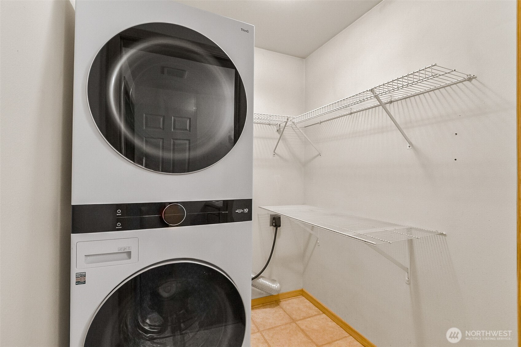 Laundry room with a stacked washer and dryer beside wall-mounted wire drying shelves.