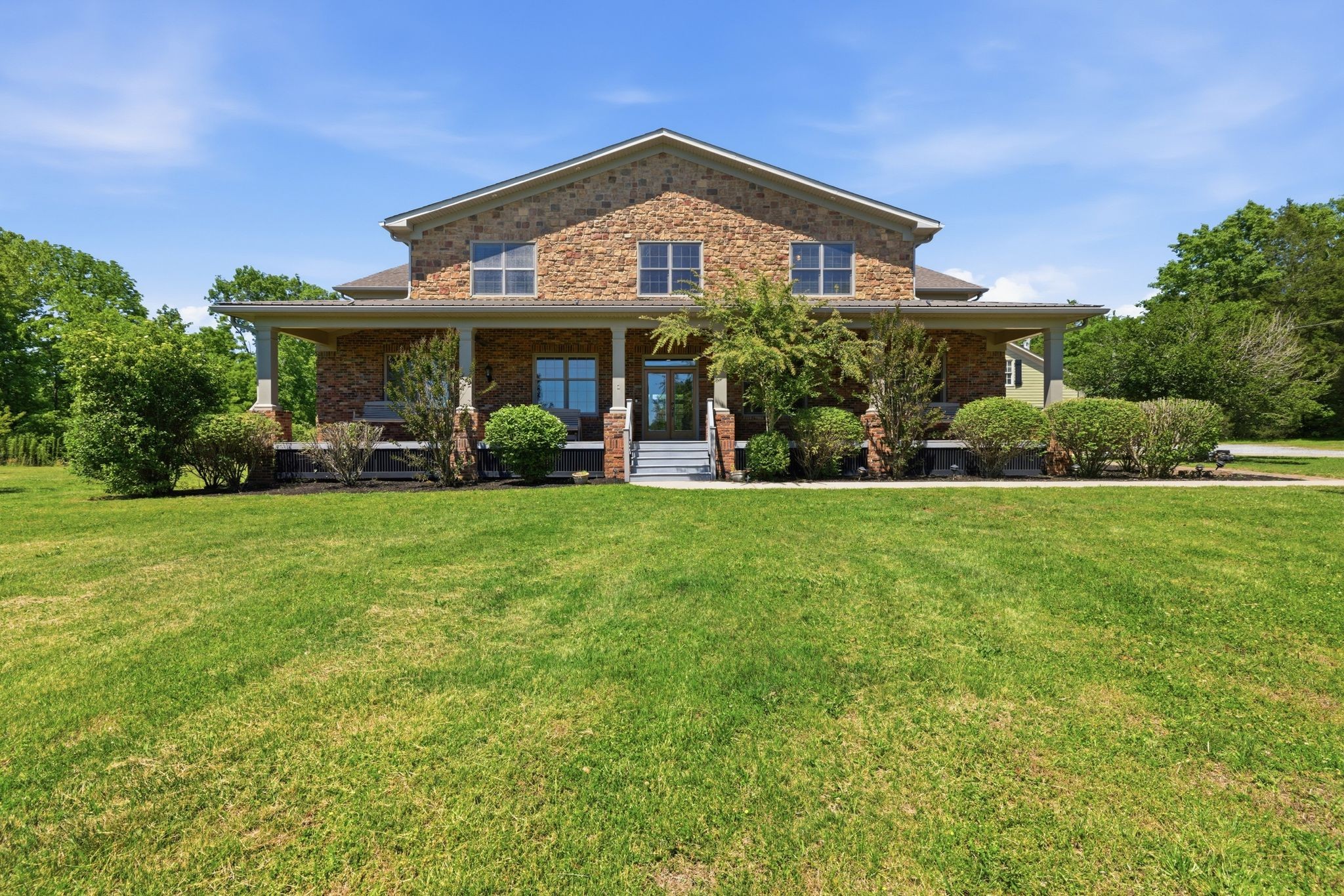 Two-story brick and stone house with a broad covered porch and wide front lawn.