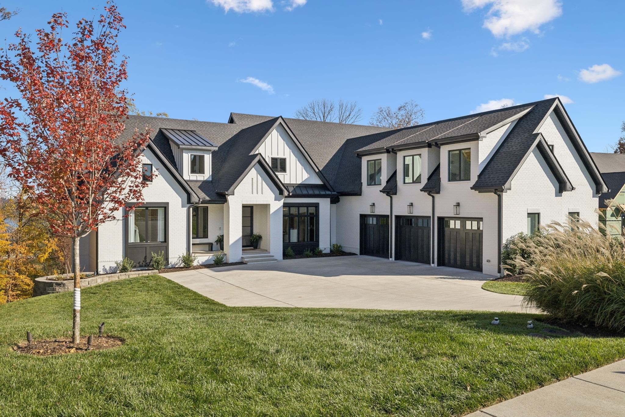 White-brick home with steep dark gables, black garage doors, and a broad driveway.