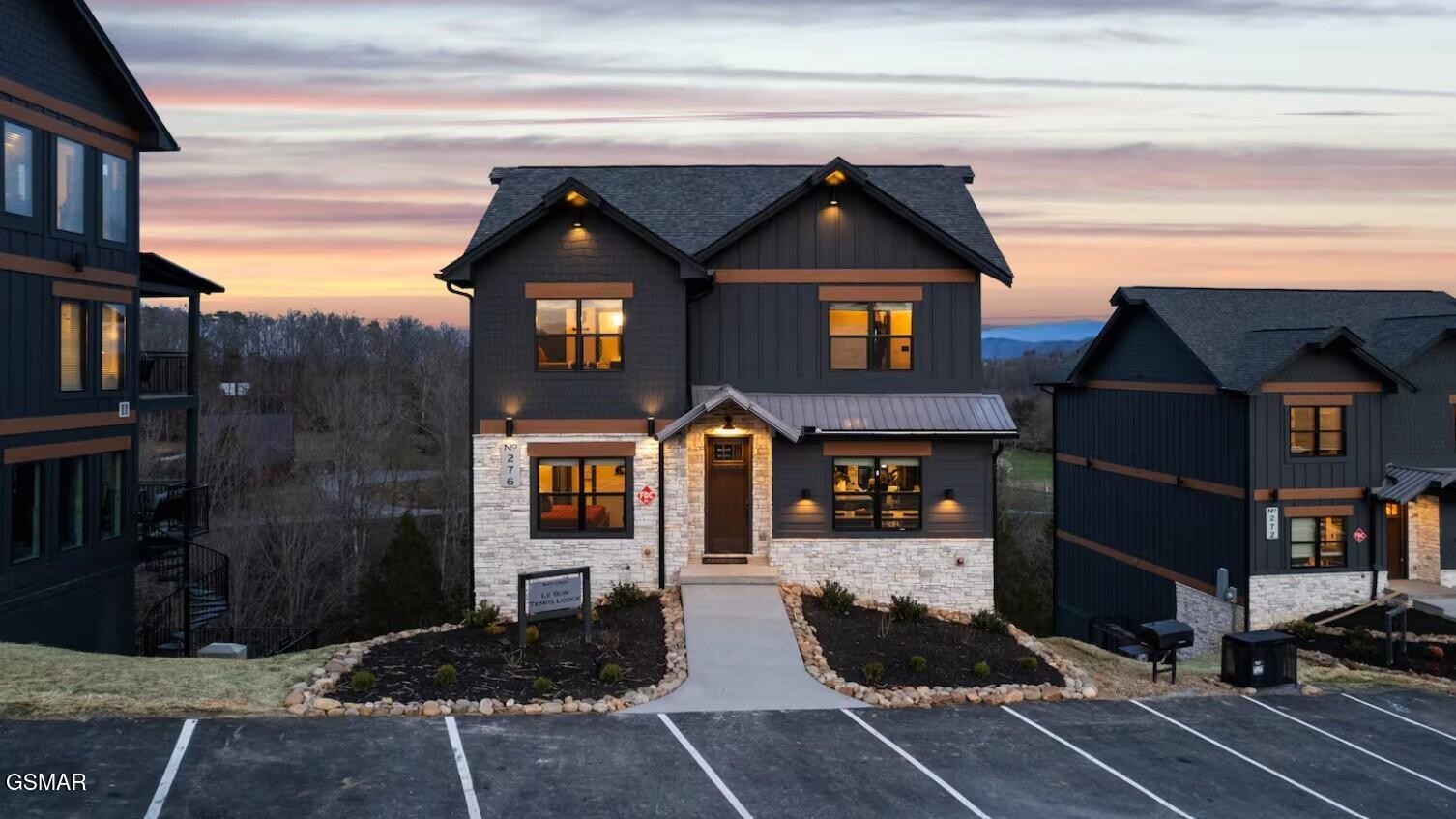 Modern dark-sided home with stone accents and a landscaped walkway at sunset.