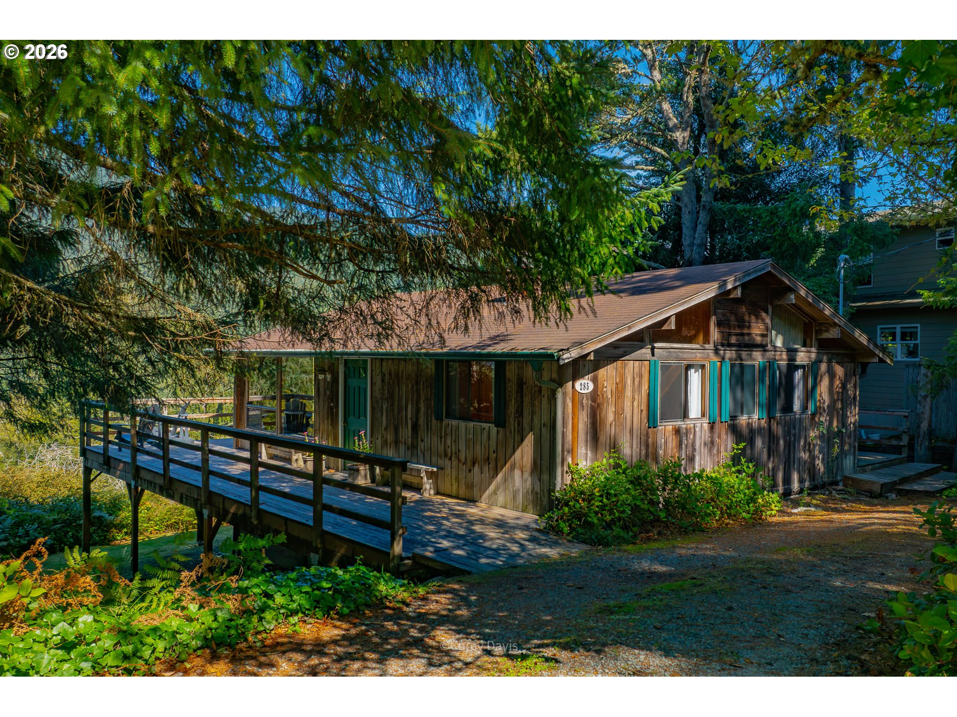 Wood-sided home among evergreens with a raised deck and teal-trimmed windows.