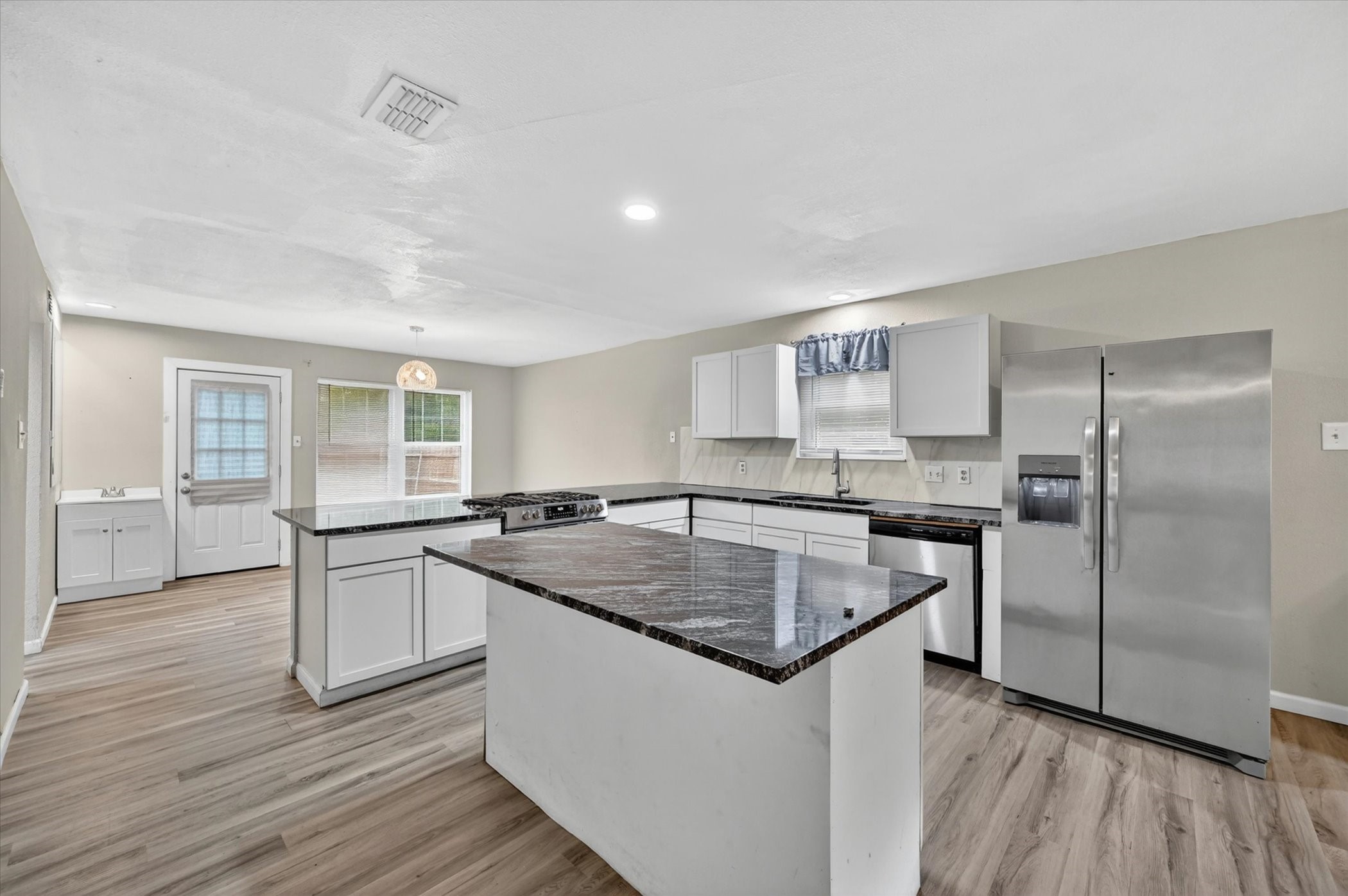 Kitchen with a large stone-topped island, white cabinetry, and stainless steel appliances.