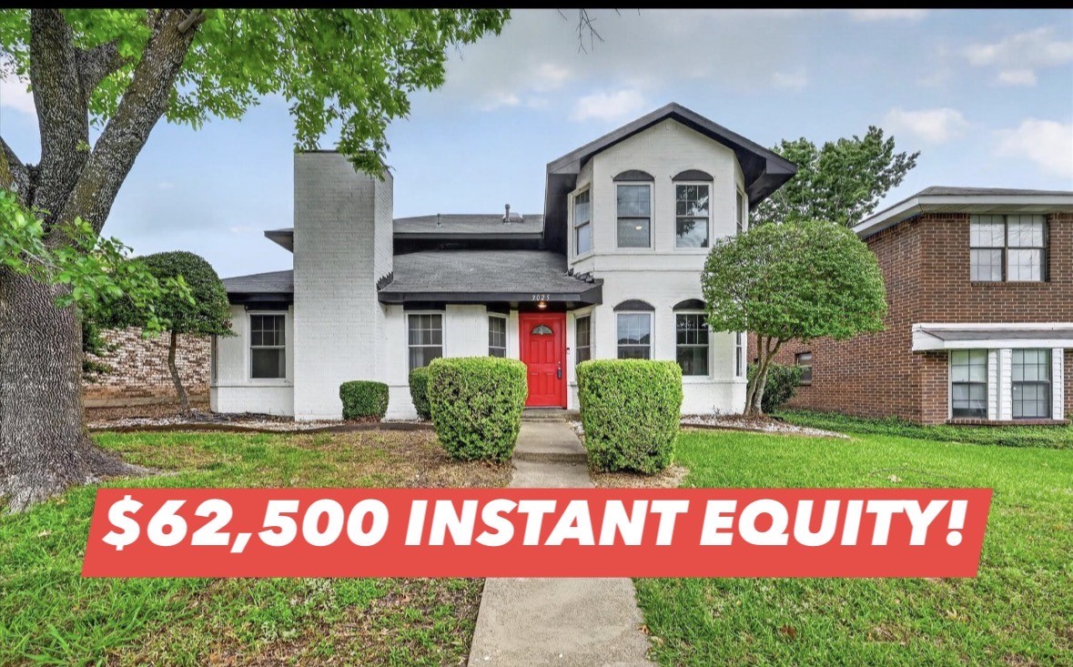 White two-story house with a bright red front door, trimmed shrubs, and a concrete walkway.