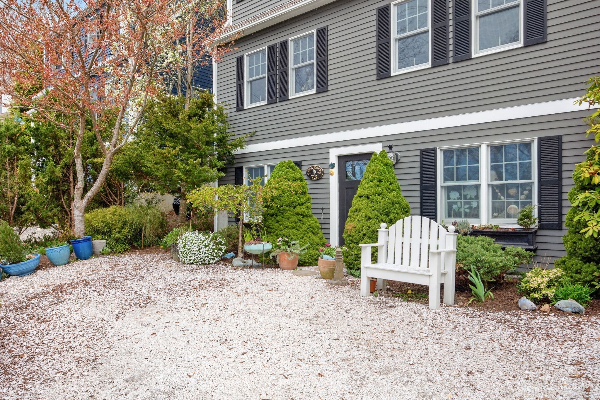 Gray house entrance with black shutters, a white Adirondack chair, and a landscaped gravel garden.