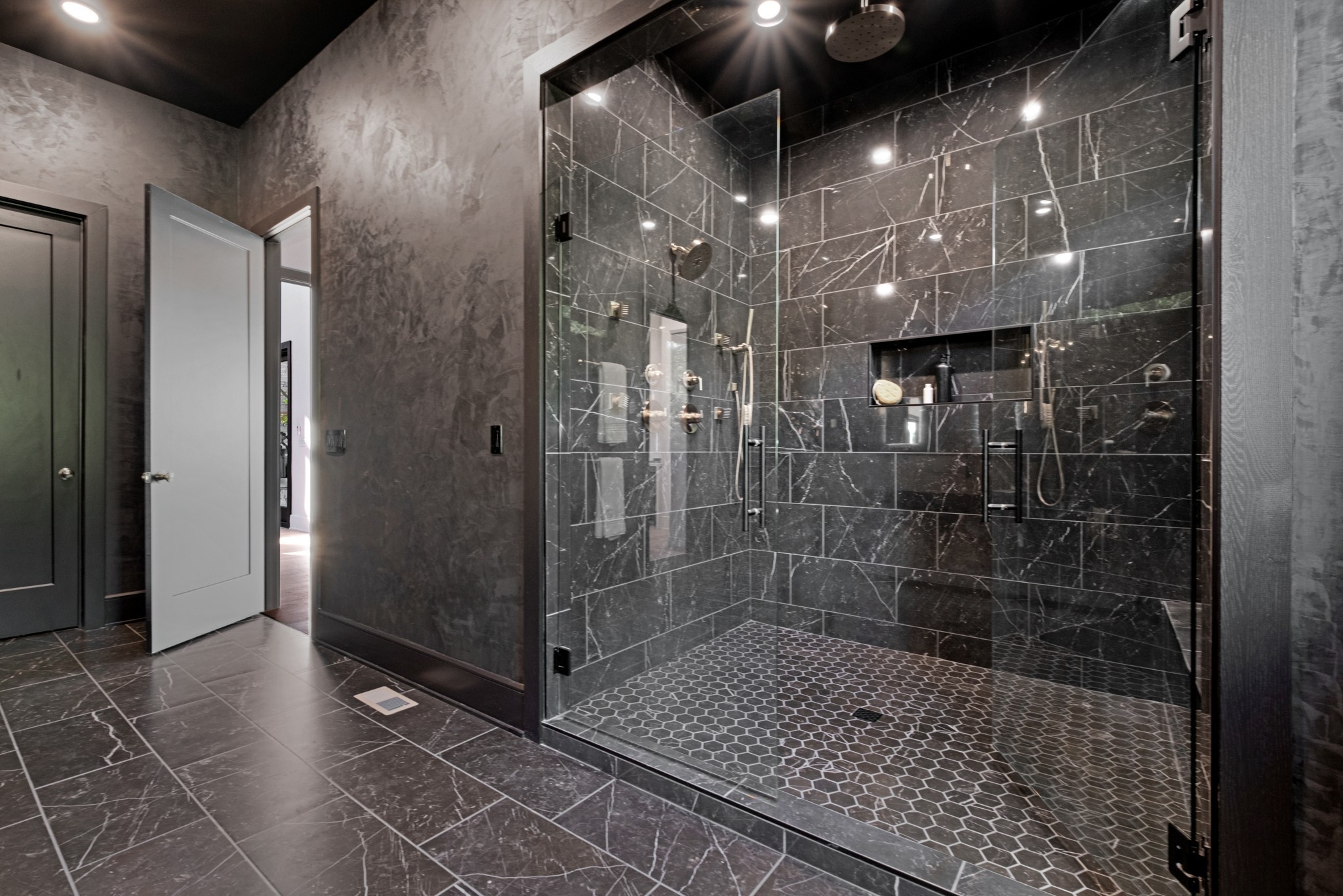 Bathroom with a glass walk-in shower, dark veined tile, multiple shower fixtures, and a hexagonal mosaic floor.