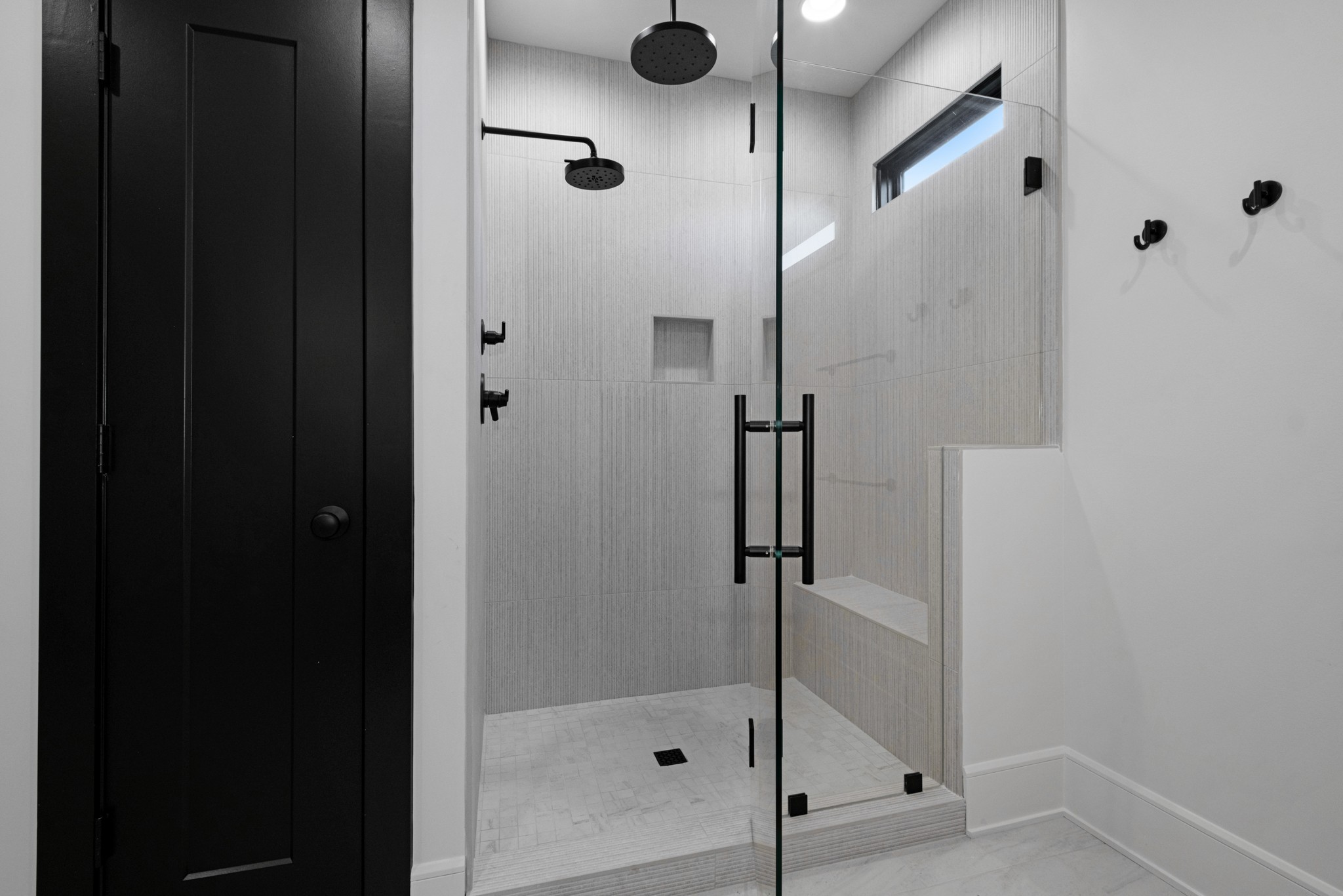 Walk-in shower with textured gray tile, black fixtures, glass enclosure, and built-in bench.