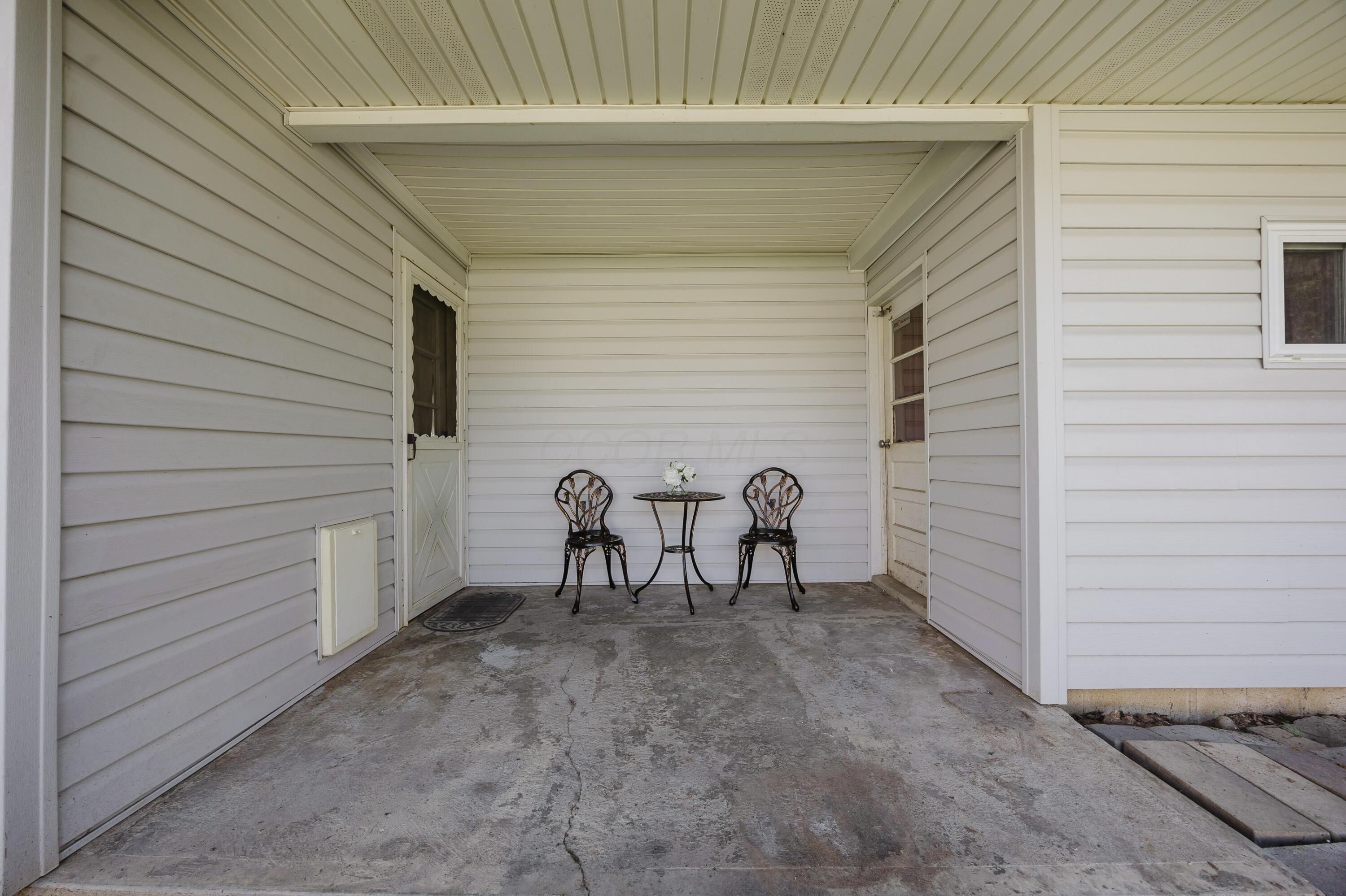 Covered porch with two metal chairs and a small round table with flowers.