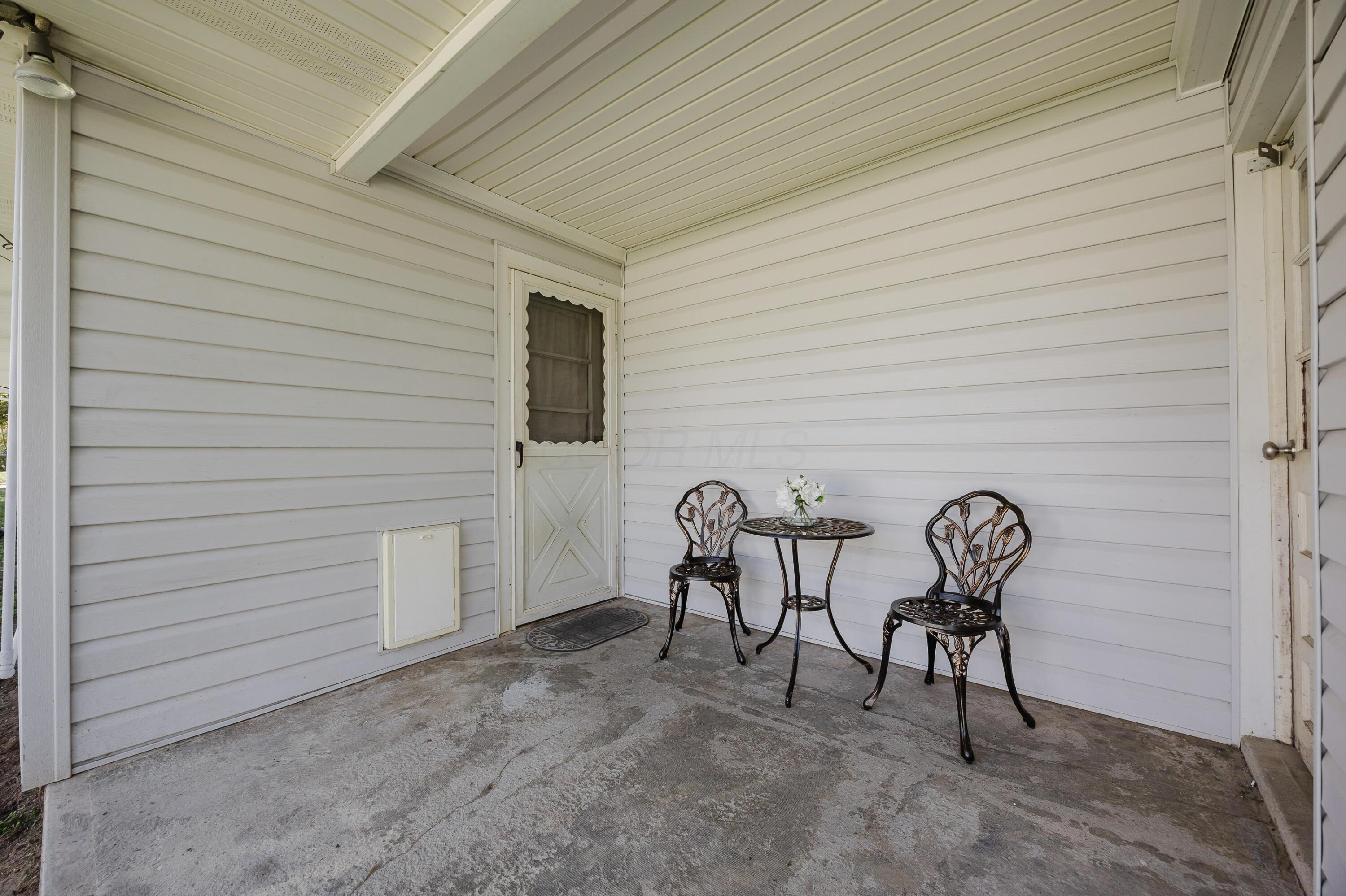 Covered porch with white siding and a black metal bistro table and chairs.