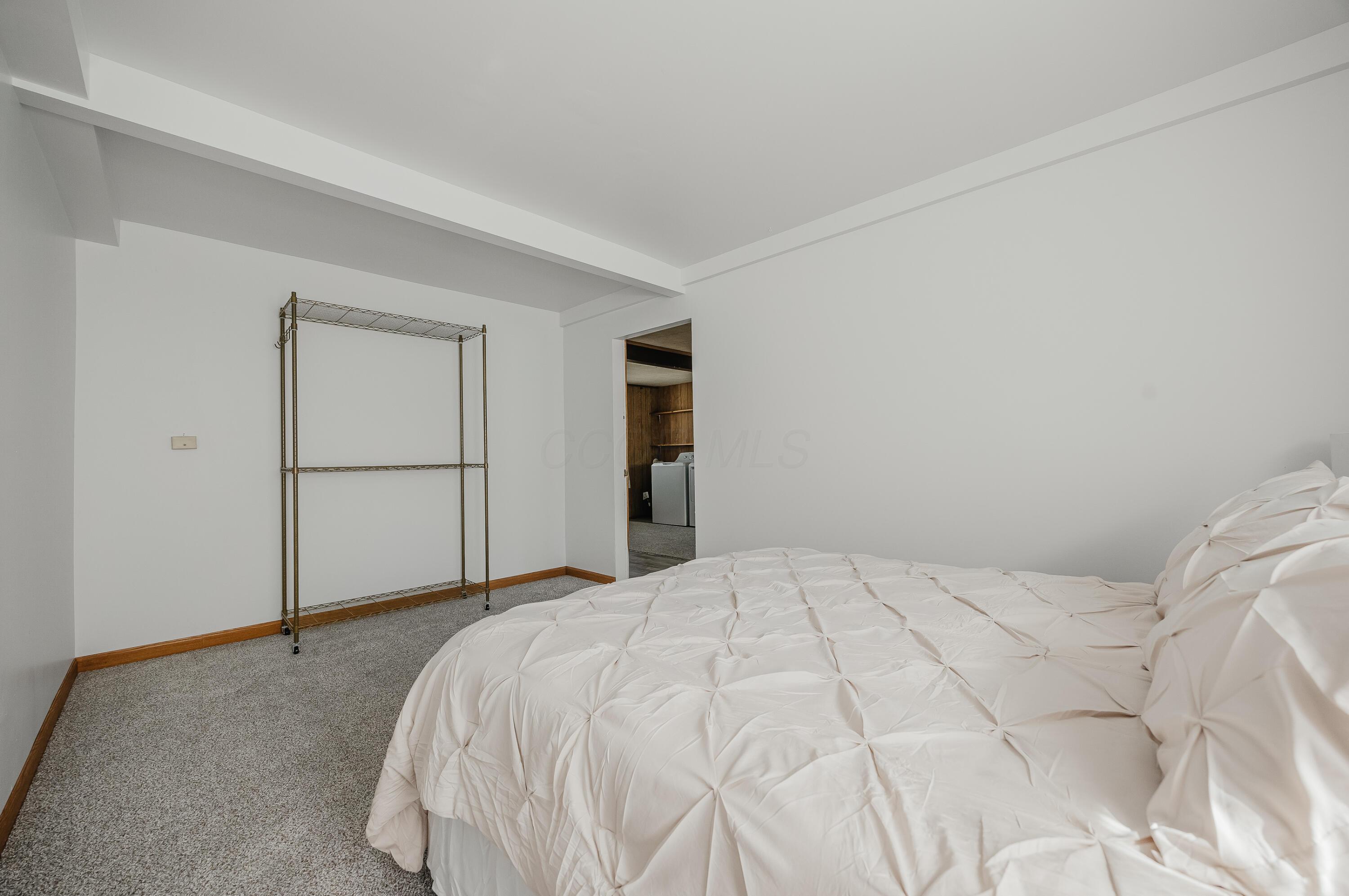 Carpeted bedroom with a large white quilted bed and a freestanding metal rack.