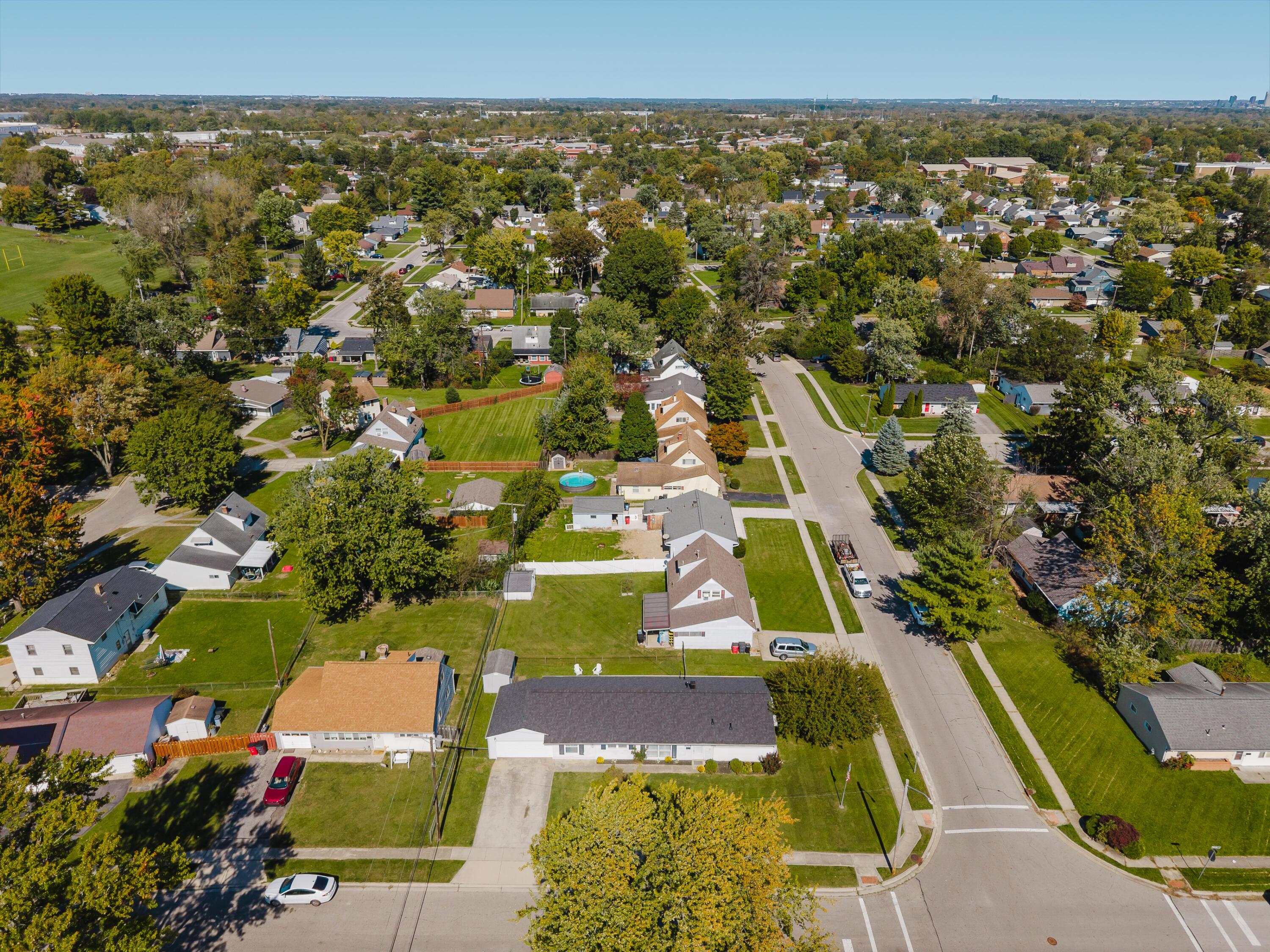 Aerial view of a tree-lined neighborhood with detached homes, intersecting streets, and a backyard pool.