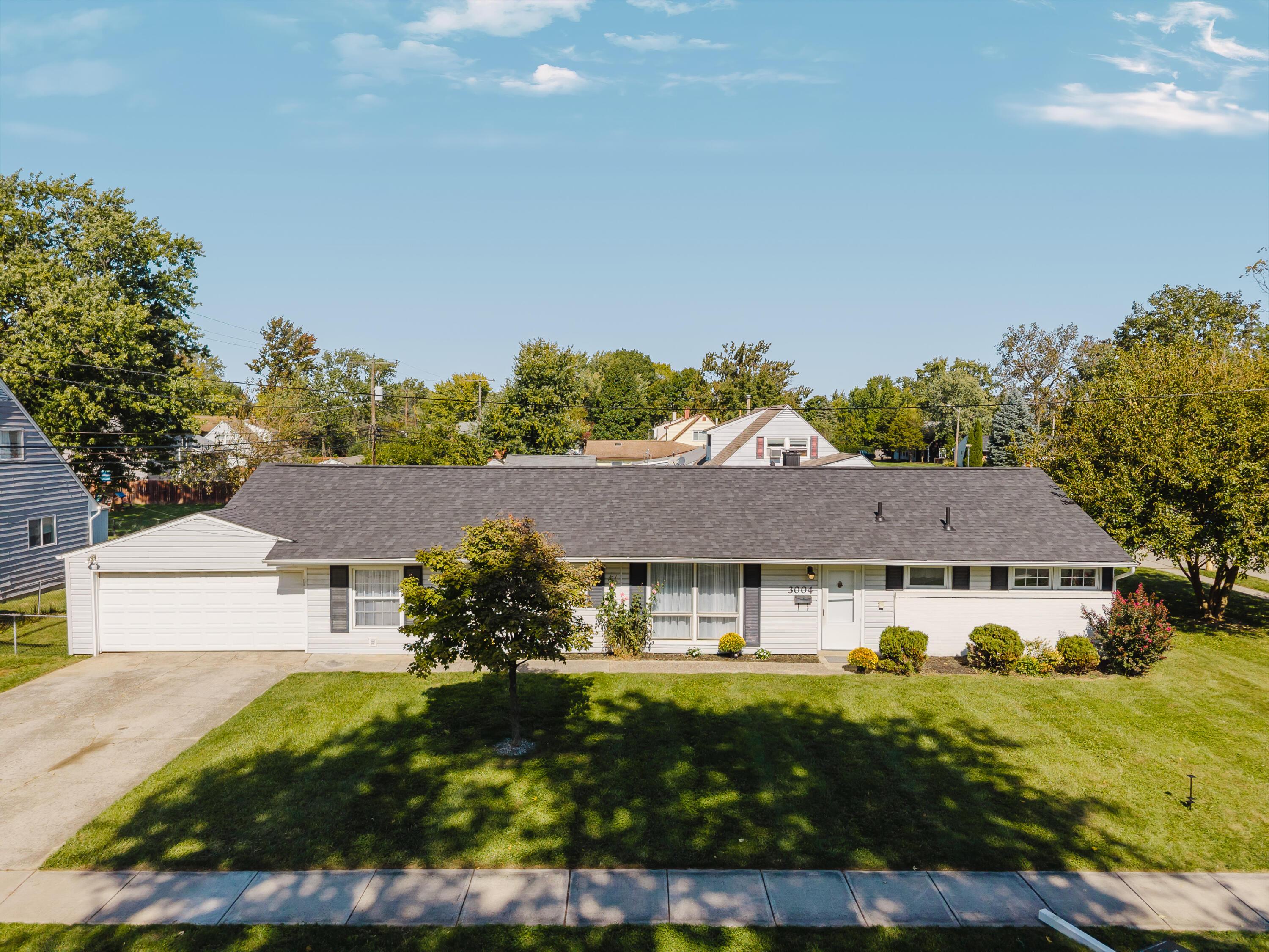 White ranch-style home with attached garage, broad lawn, and mature trees.