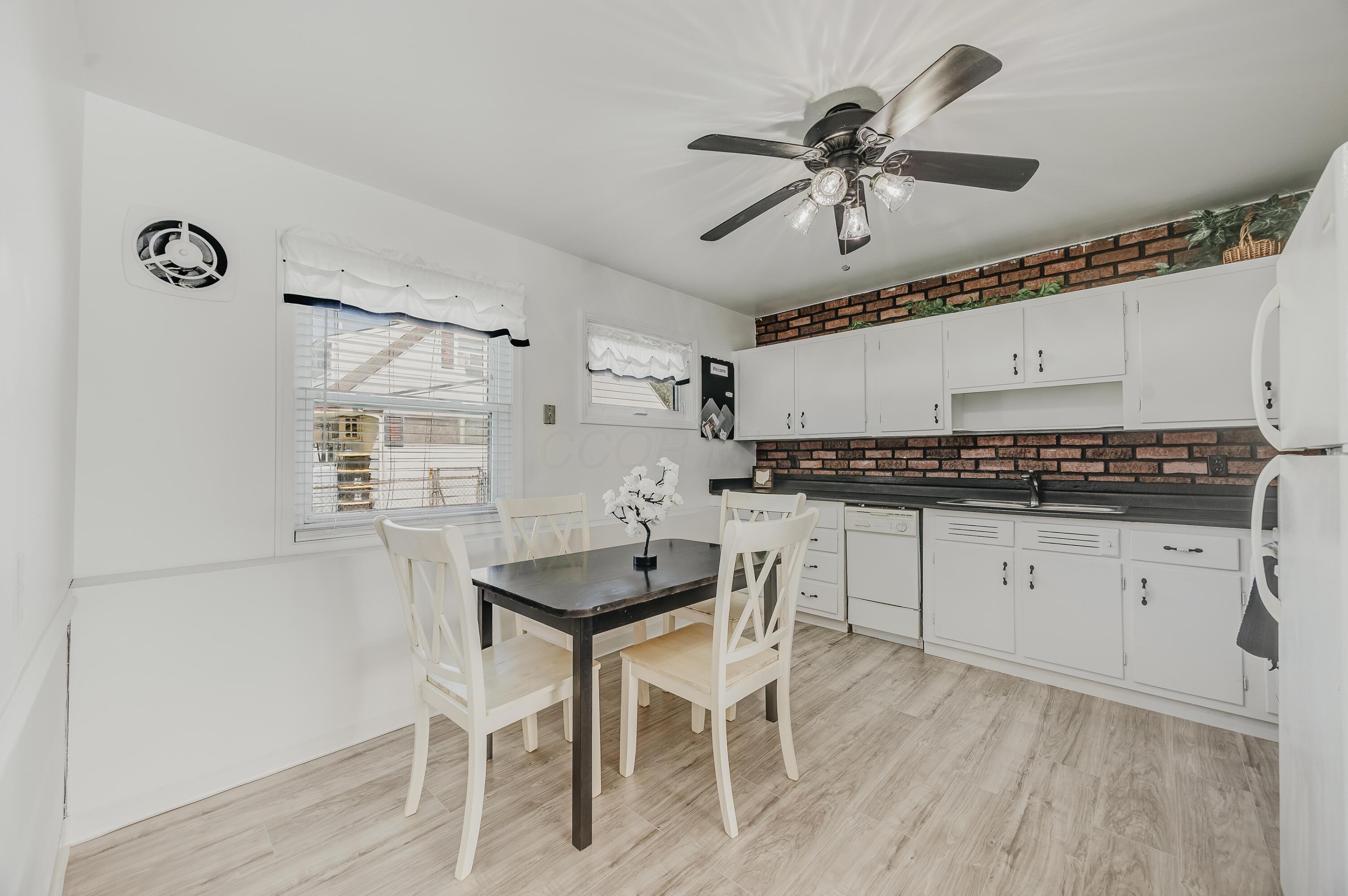 Kitchen and dining area with white cabinets, brick backsplash, and a black table with white chairs.
