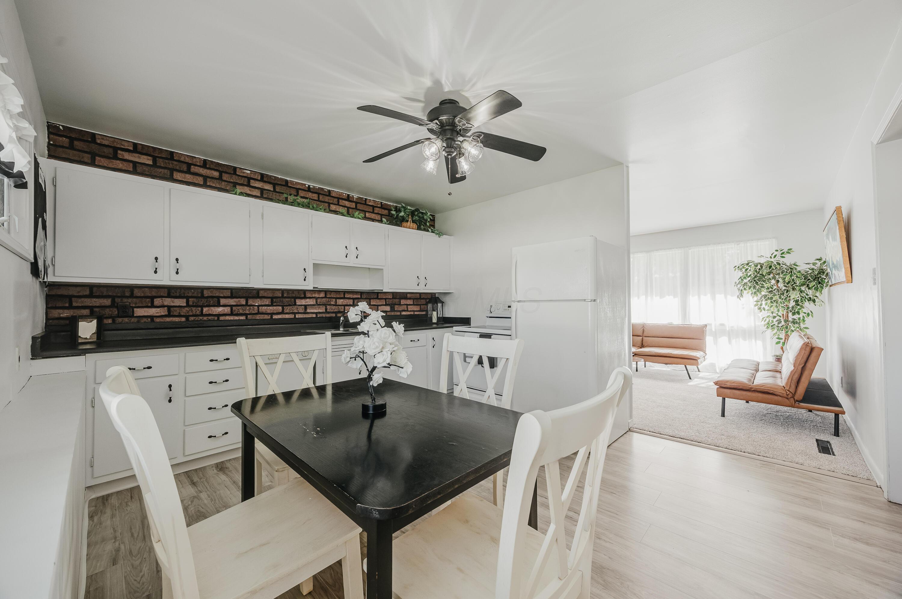 Kitchen and dining area with white cabinetry, brick backsplash, and an adjoining living room.