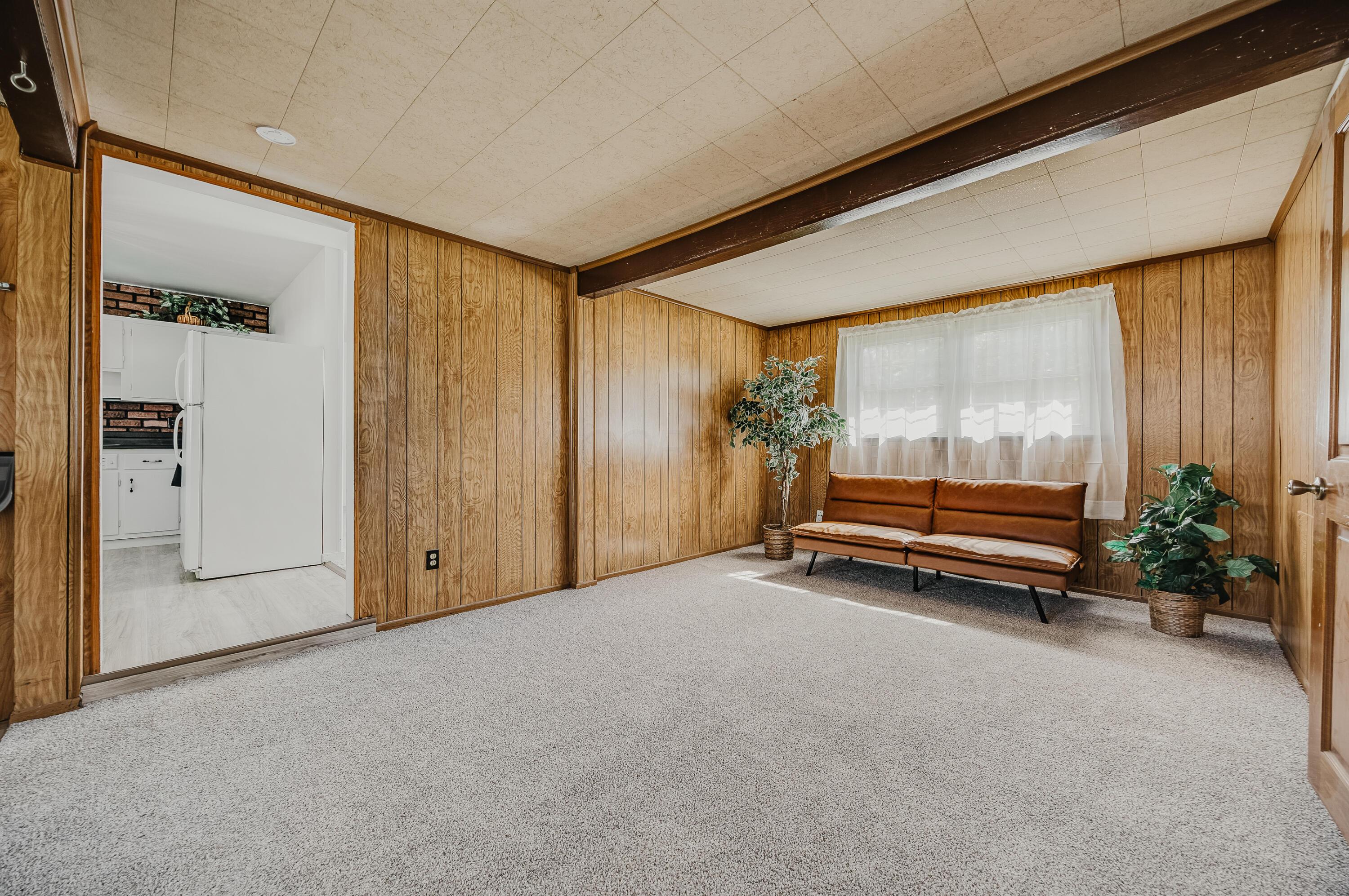 Living room with wood-paneled walls, a brown sofa, and a view into the kitchen.