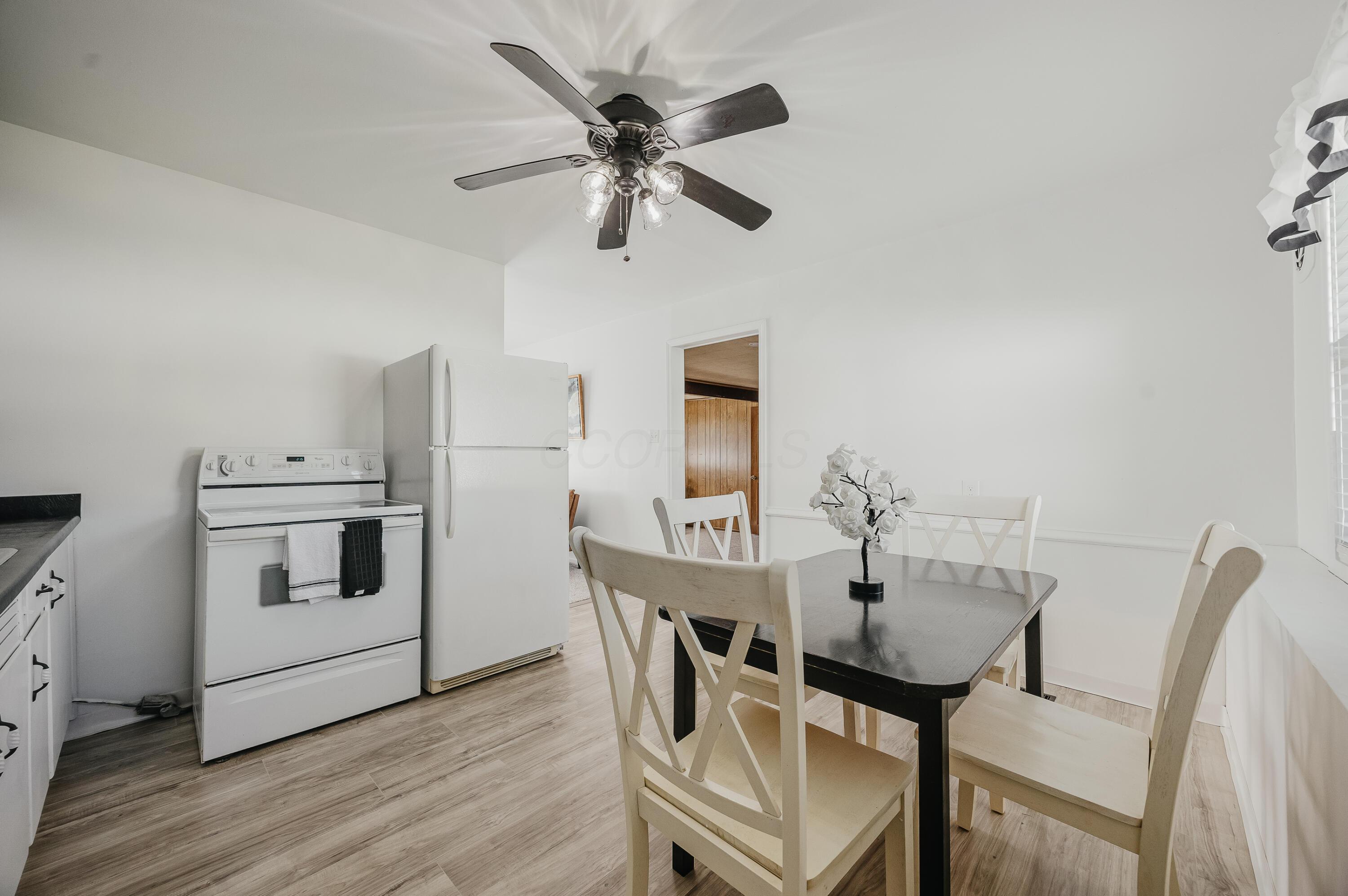 Dining area with a black table, white chairs, refrigerator, and range.