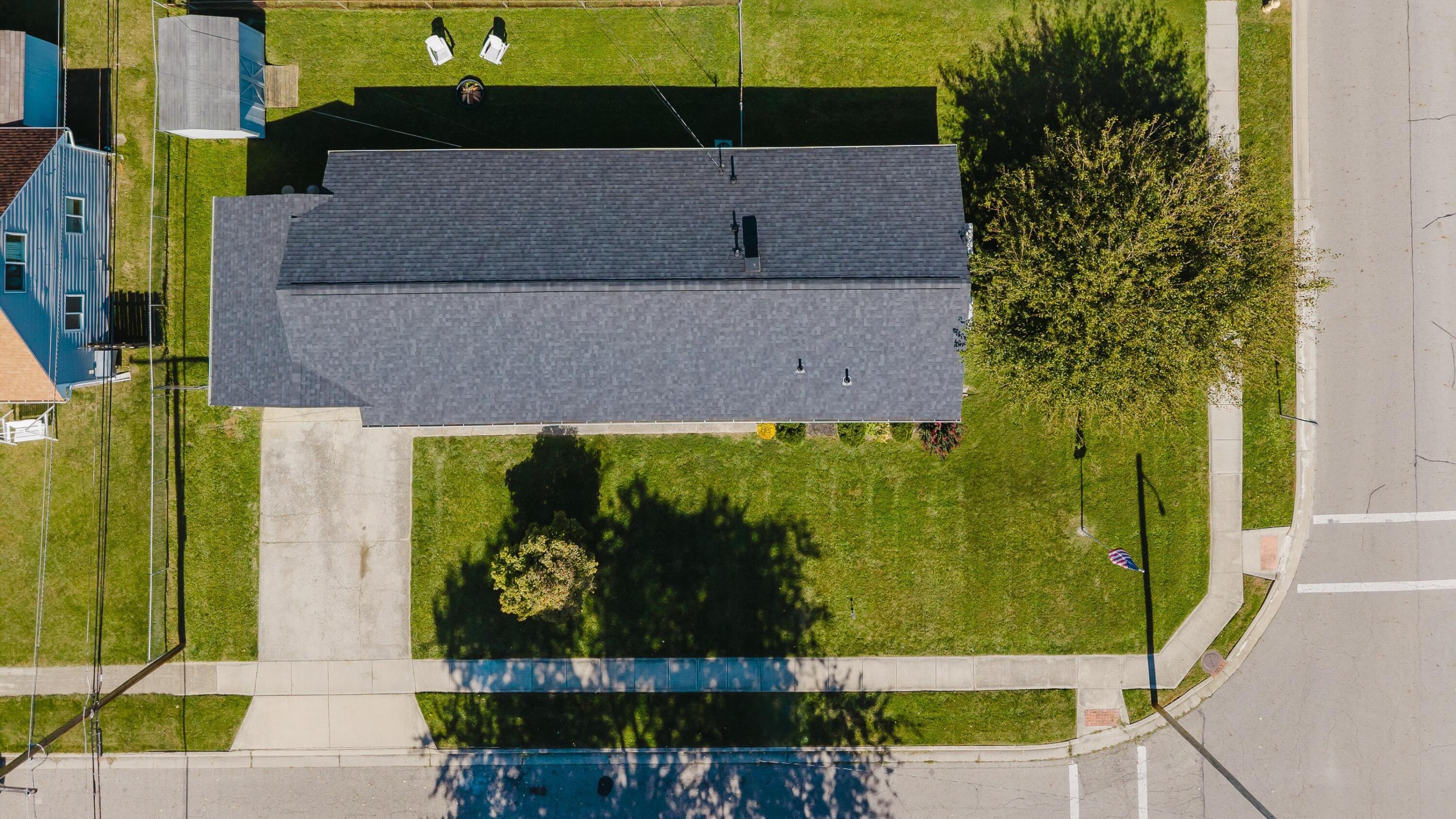 Aerial view of a home with a gray shingle roof, lawn, and driveway on a corner lot.