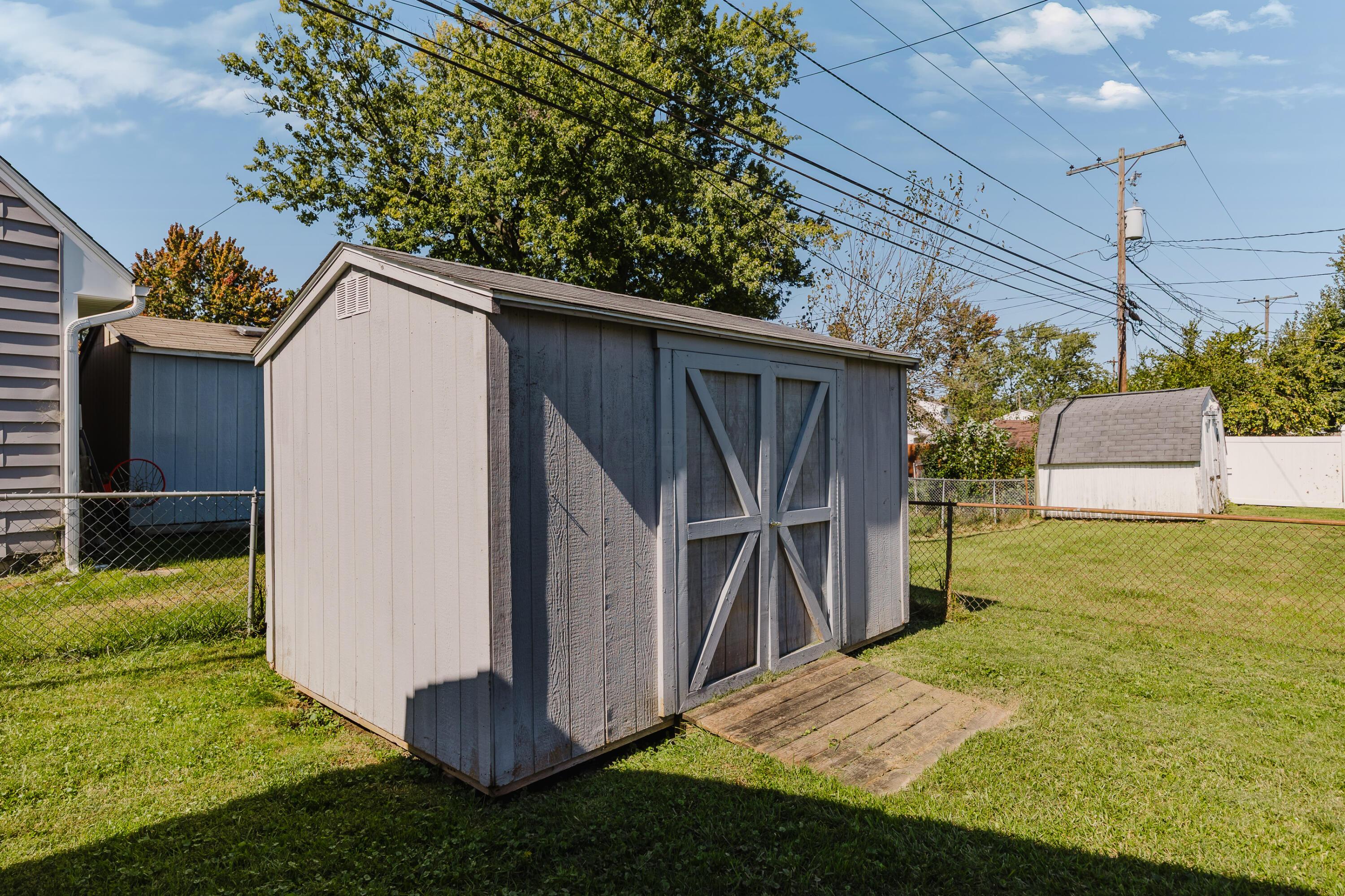 Large gray storage shed with barn-style doors in a fenced grassy yard.