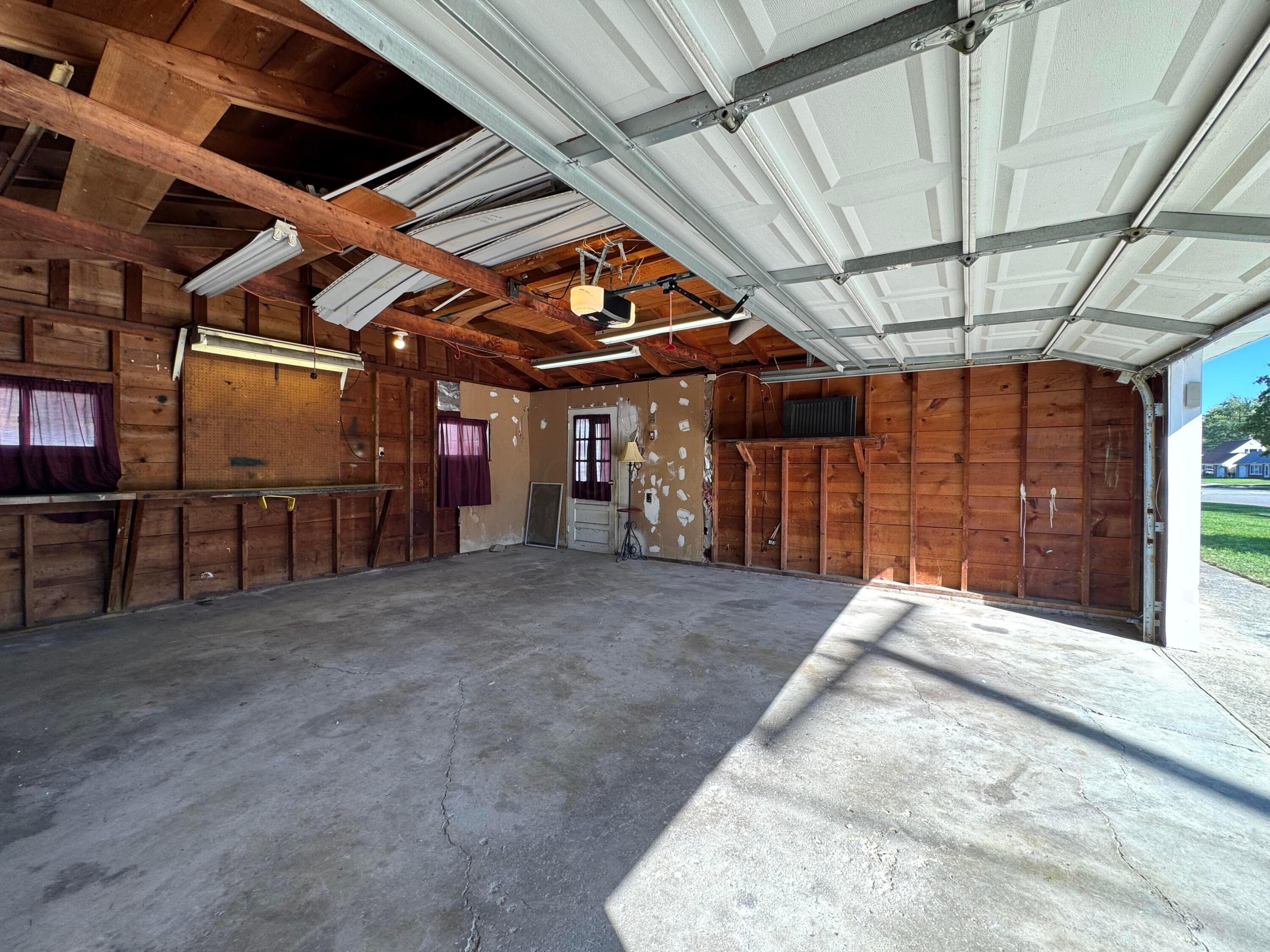 Open garage with exposed wood framing, a concrete floor, and a raised sectional door.