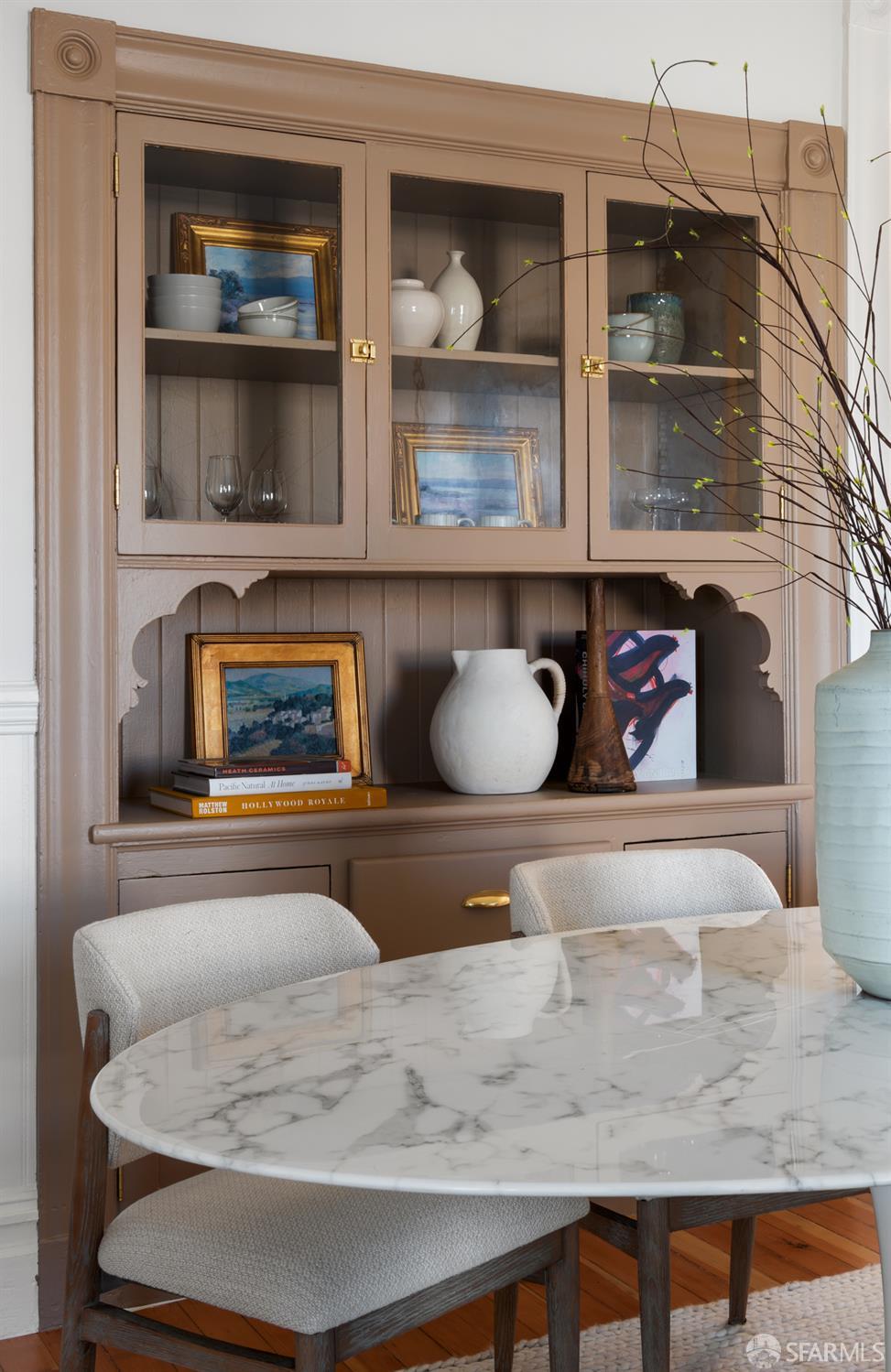Dining area with a glass-front built-in hutch, marble-patterned table, and upholstered chairs.