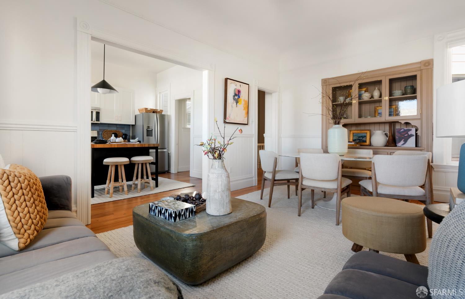 Living and dining room opening to a kitchen, with hardwood floors and a built-in display cabinet.
