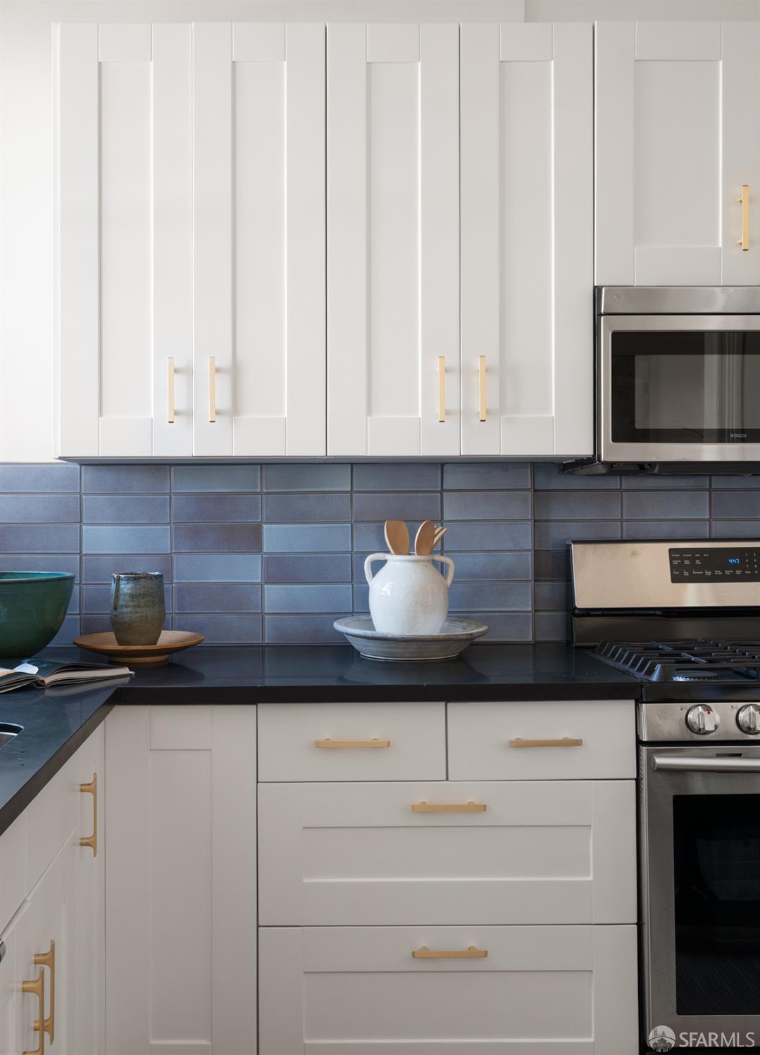 Kitchen with white cabinets, brass hardware, blue tile backsplash, and stainless steel appliances.