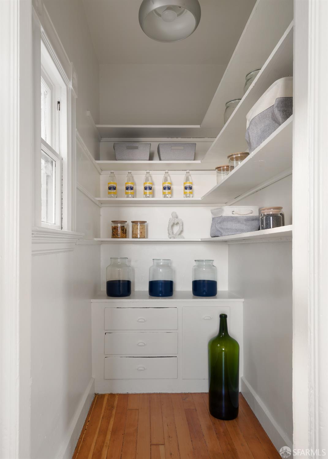 Pantry with white built-in shelves and drawers, glass jars, and a window.