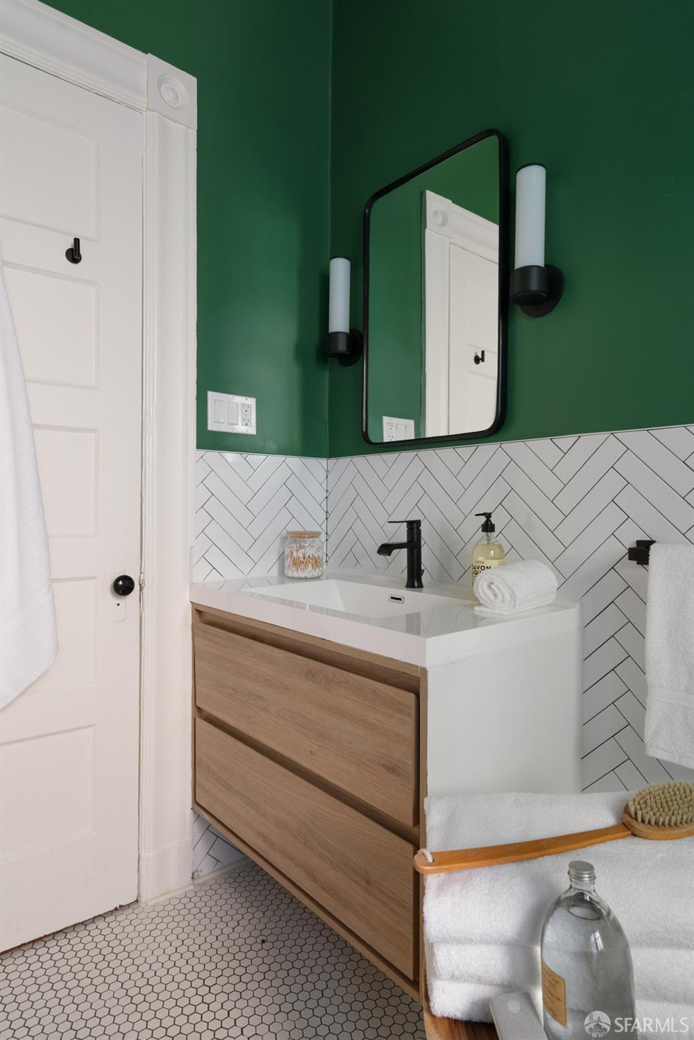Bathroom with a wood-front vanity, green walls, and white herringbone tile.