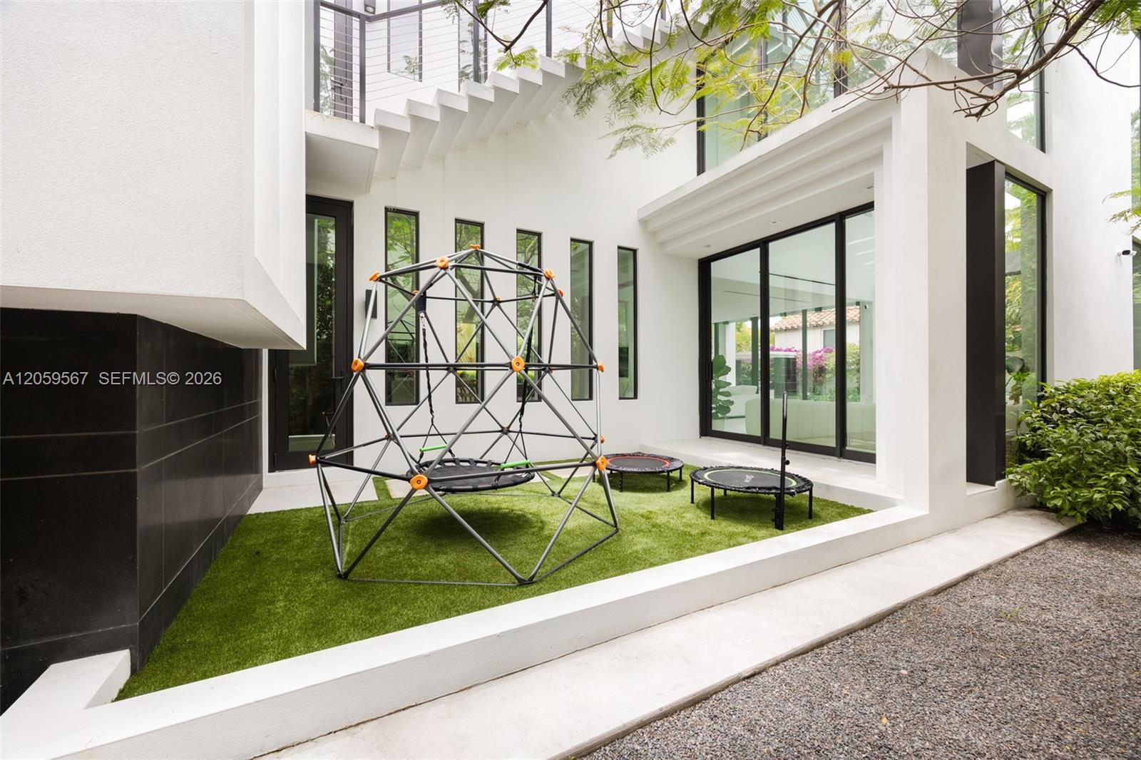Modern home courtyard with artificial turf, a climbing dome, and two small trampolines.