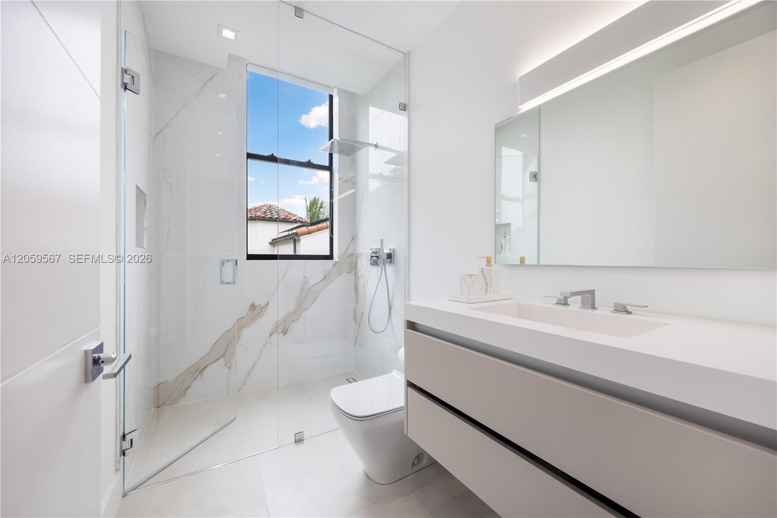 Modern bathroom with a marble-look glass shower, large window, and floating vanity.