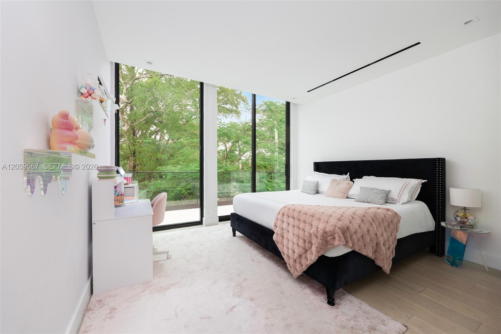Bedroom with a black bed, blush-pink throw, and floor-to-ceiling windows overlooking leafy trees.