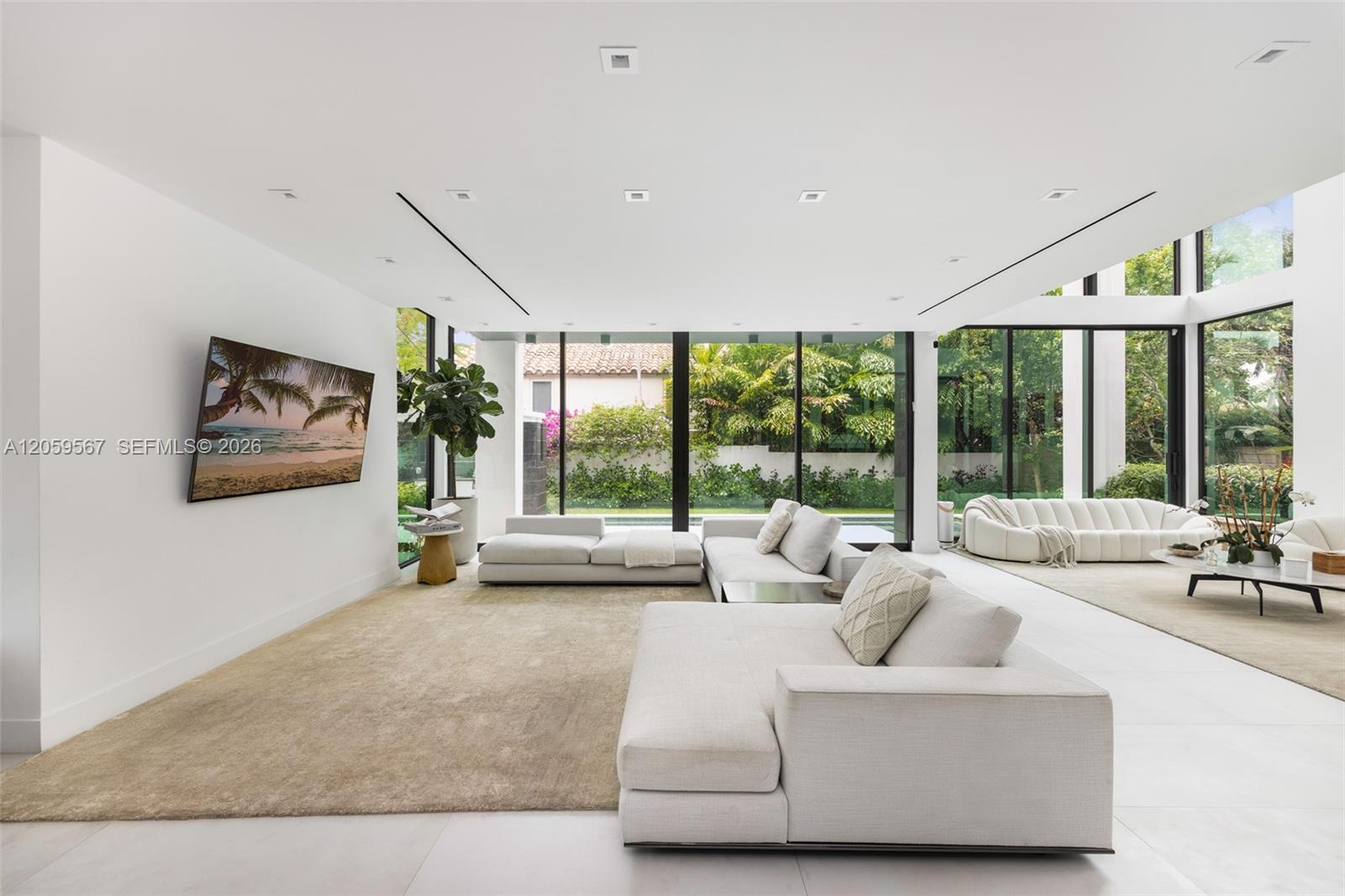 Modern living room with white sectional sofas and floor-to-ceiling garden-facing windows.