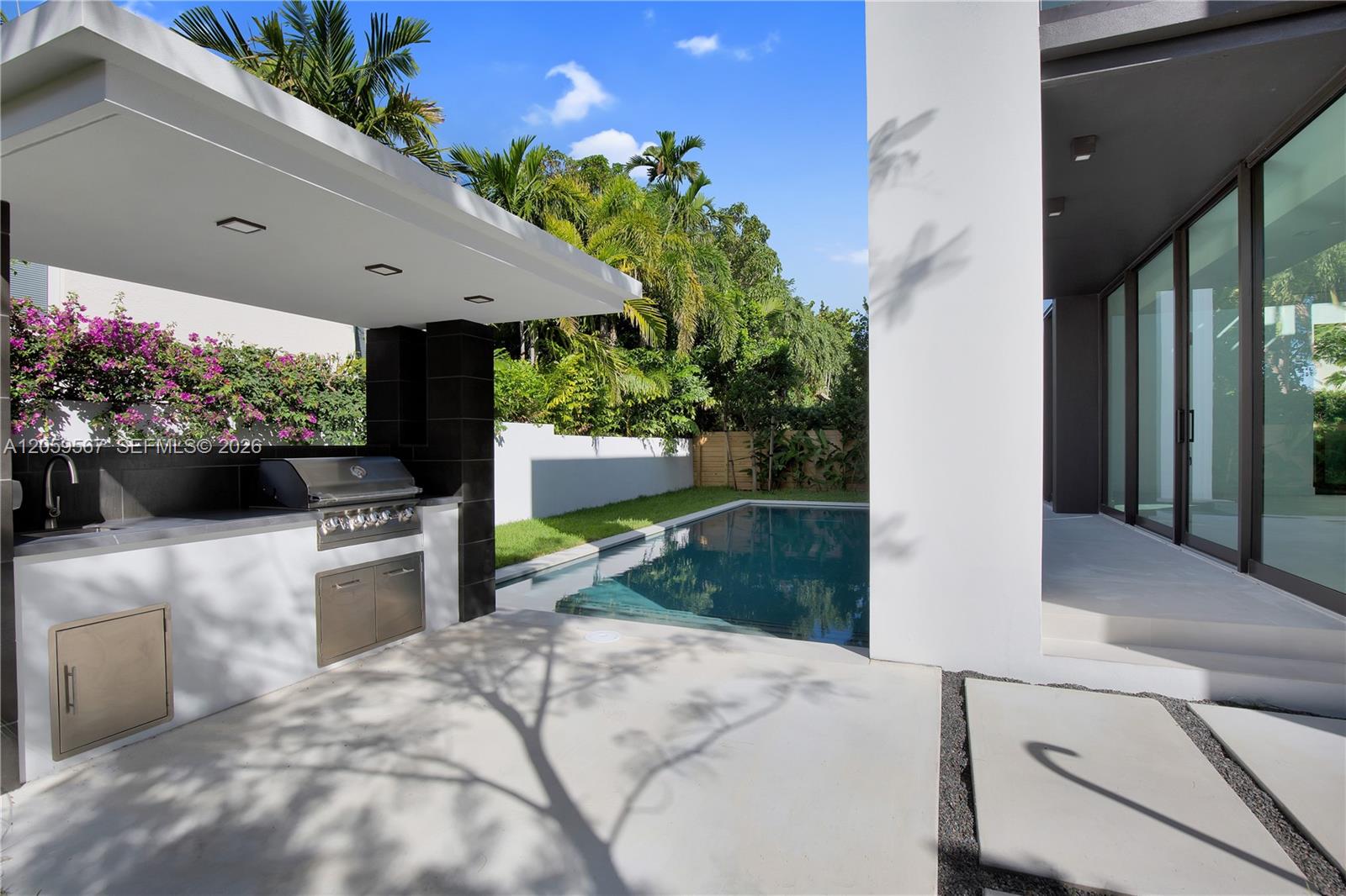 Modern home’s poolside patio with a covered outdoor kitchen and built-in grill.