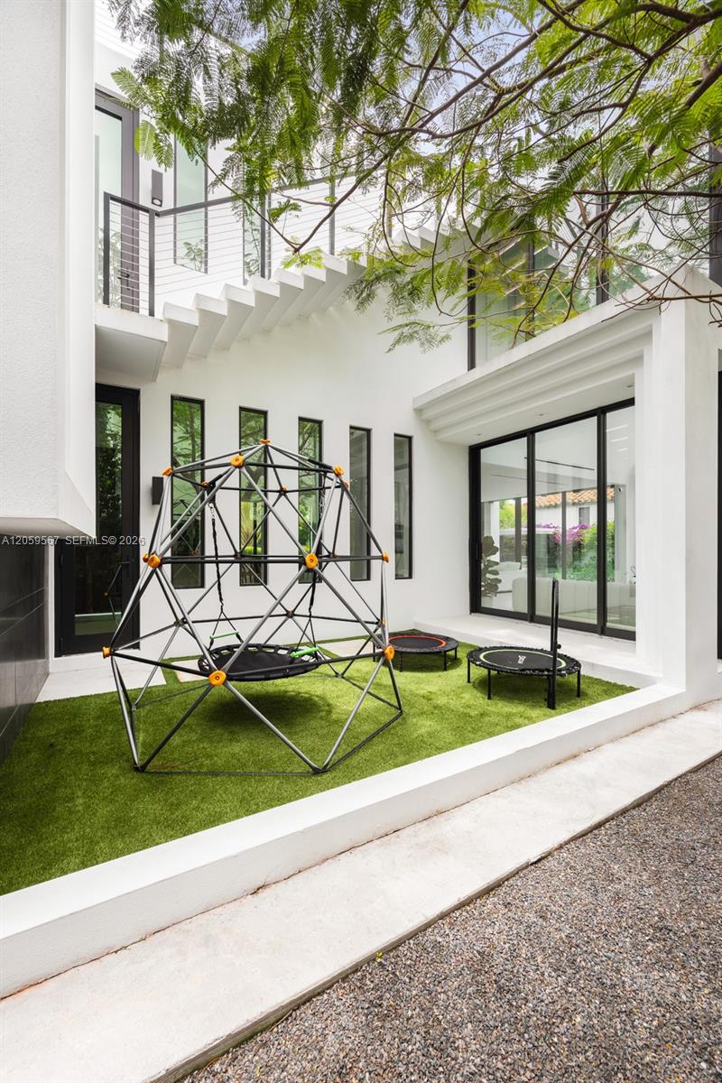 Modern home's courtyard with artificial grass, a climbing dome, and two mini trampolines.
