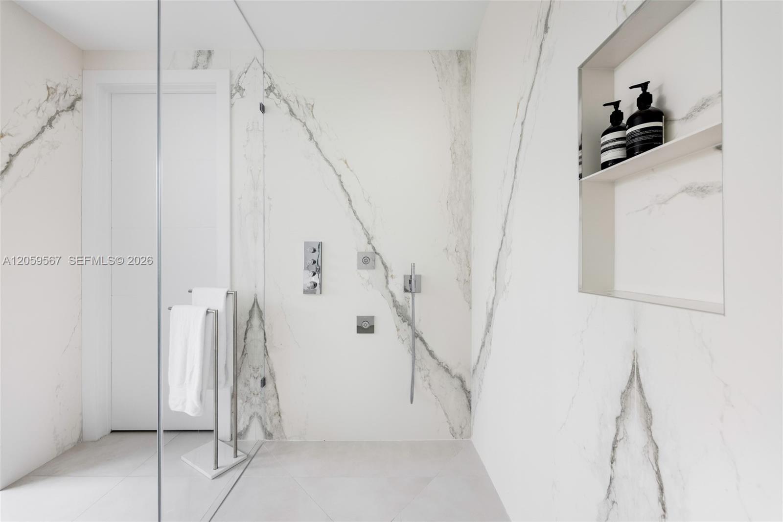 Marble bathroom shower with glass partition, chrome fixtures, towel stand, and recessed shelf.