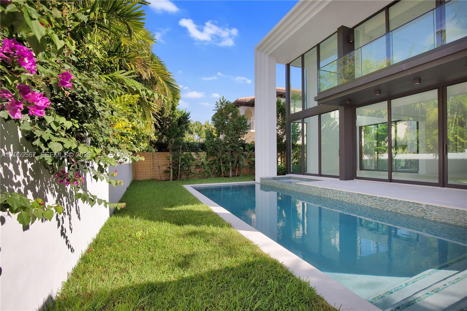 Modern glass-fronted home beside a swimming pool, with tropical landscaping and pink bougainvillea.