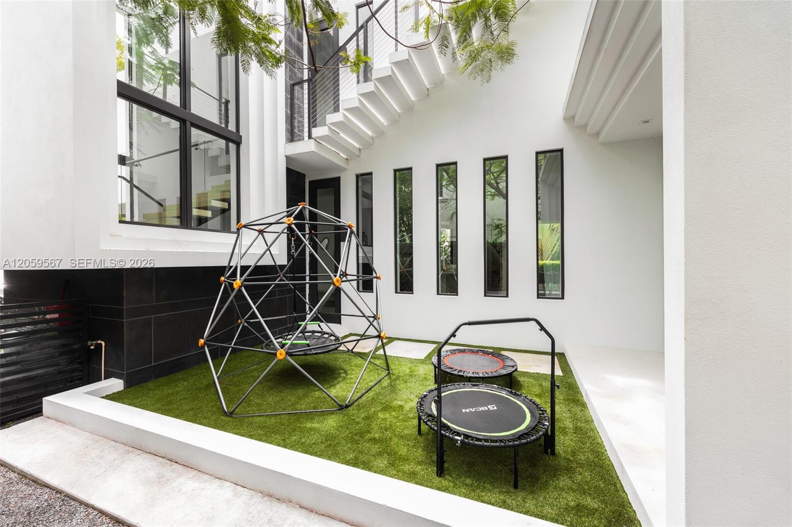 Modern home courtyard with artificial turf, a climbing dome, two trampolines, and an exterior staircase.