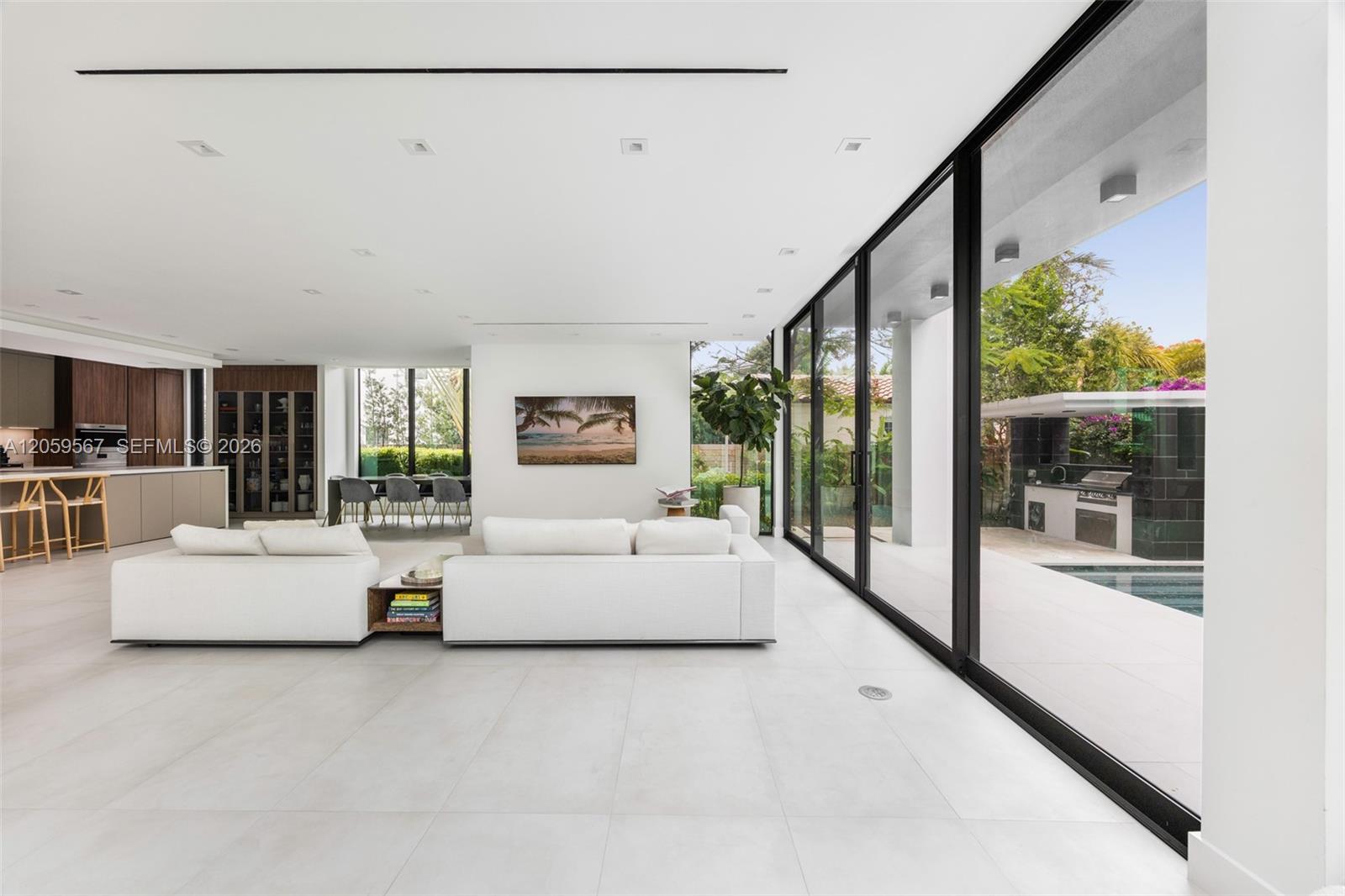 Open-plan living room with white sofas, floor-to-ceiling glass doors, and a poolside view.