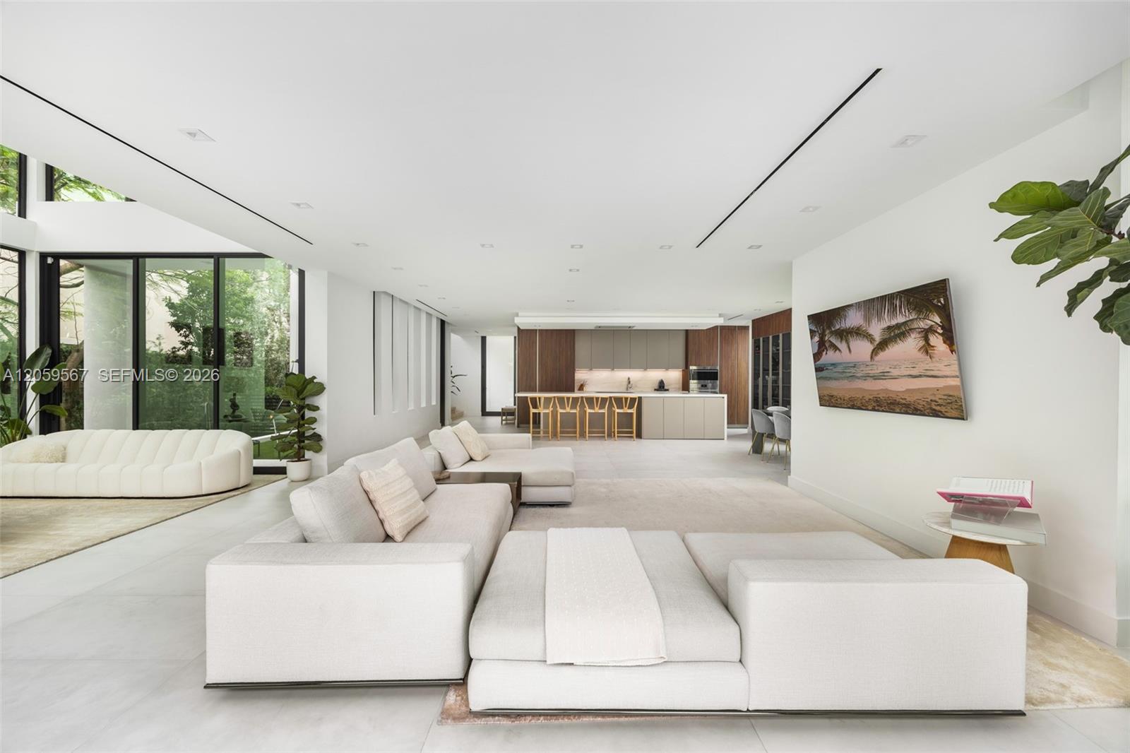Open-plan living room with white sectional sofas, large windows, and a wood-accented kitchen.