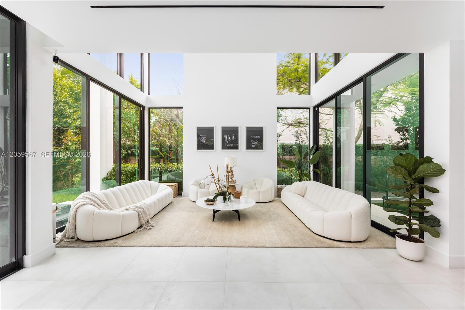 Double-height living room with curved white sofas and floor-to-ceiling windows overlooking greenery.
