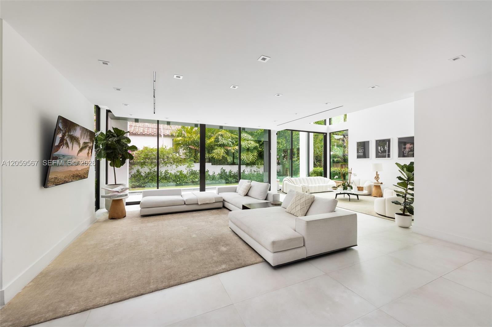 Bright living room with white sectional sofas and floor-to-ceiling garden-view windows.