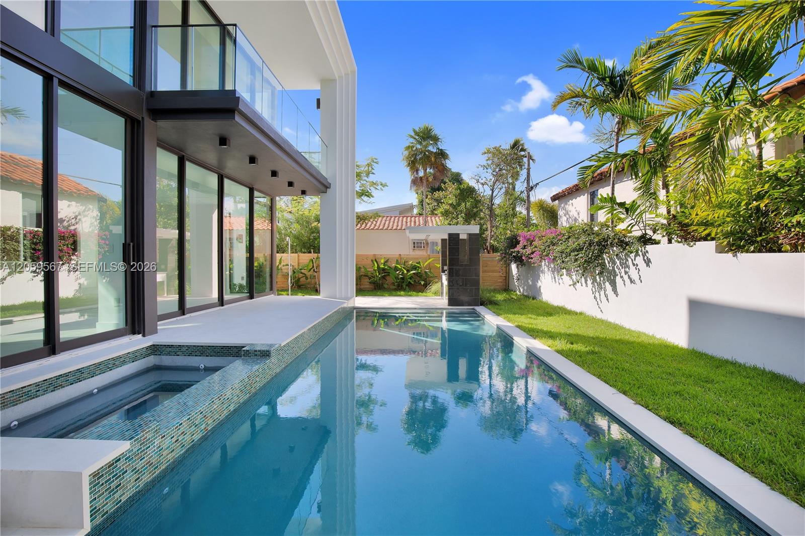 Backyard pool beside a modern glass-fronted home, with a raised tiled spa and tropical landscaping.