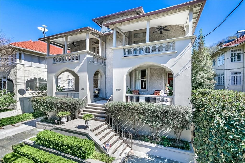 White stucco residence with arched porches, upper balconies, and a landscaped front stairway.