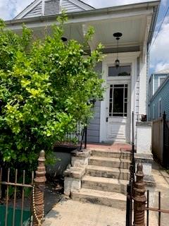 House entrance with a white door, covered porch, stone steps, and leafy shrubs.