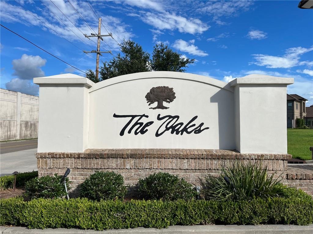 The Oaks neighborhood entrance sign with a tree emblem, brick base, and landscaped shrubs.
