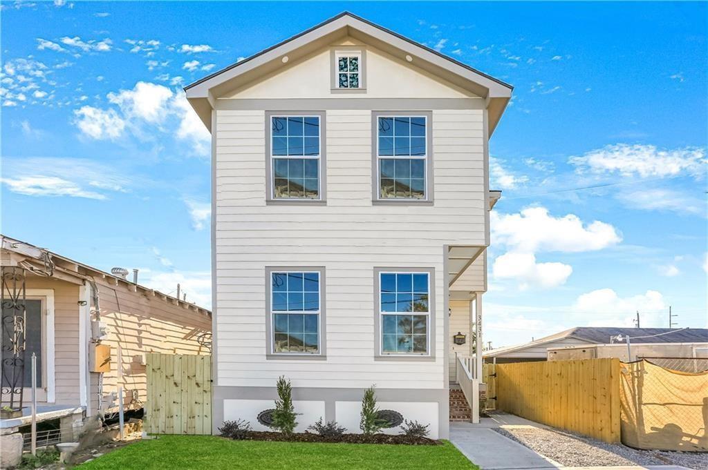 White two-story house with a steep gabled roof, gray-trimmed windows, and a fenced lawn.