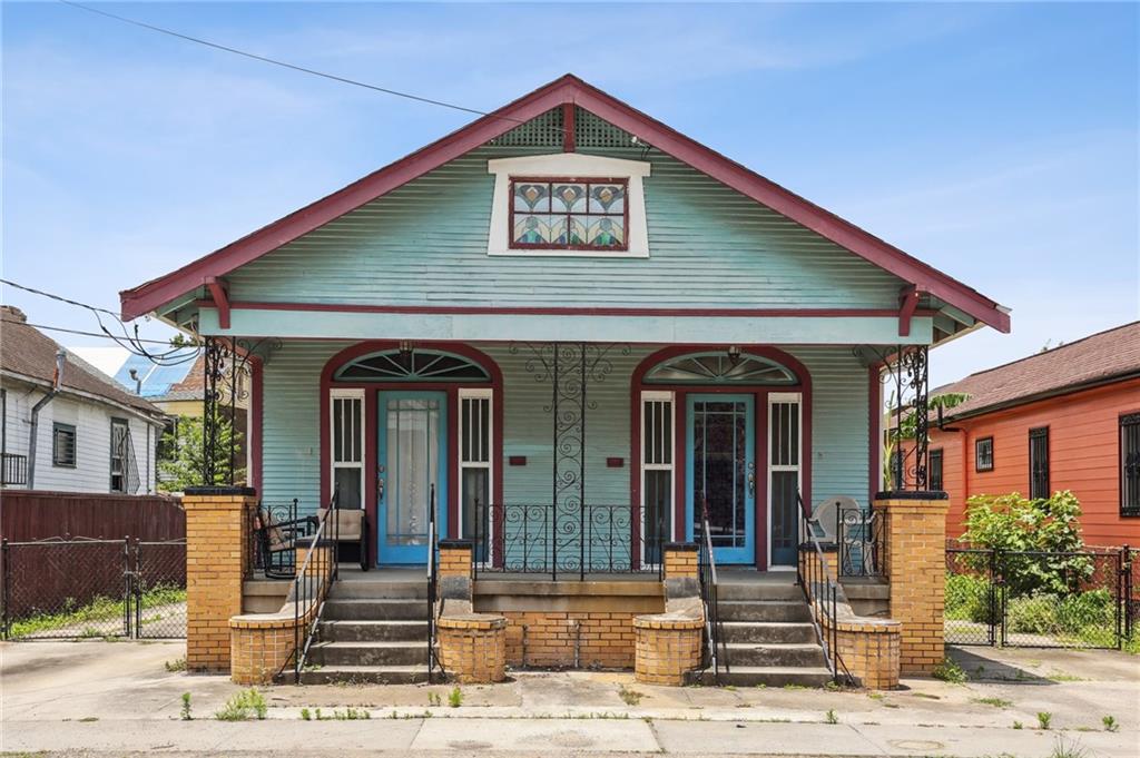 Mint-green home with red trim, twin blue doors, arched windows, and brick front steps.