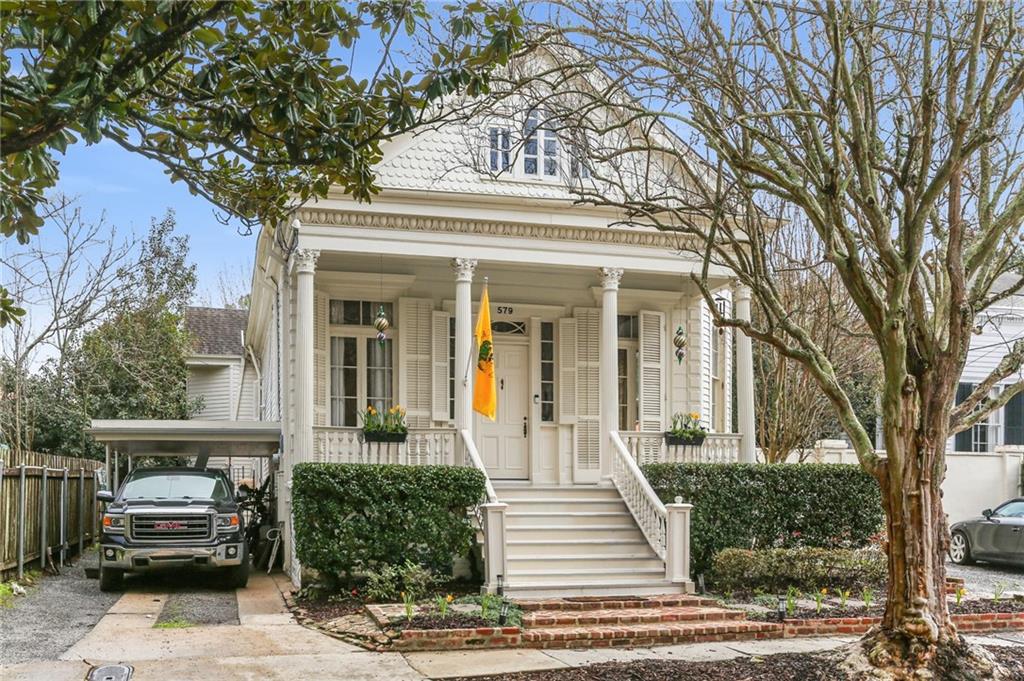 White house with a columned porch, broad front steps, and a vehicle under the carport.