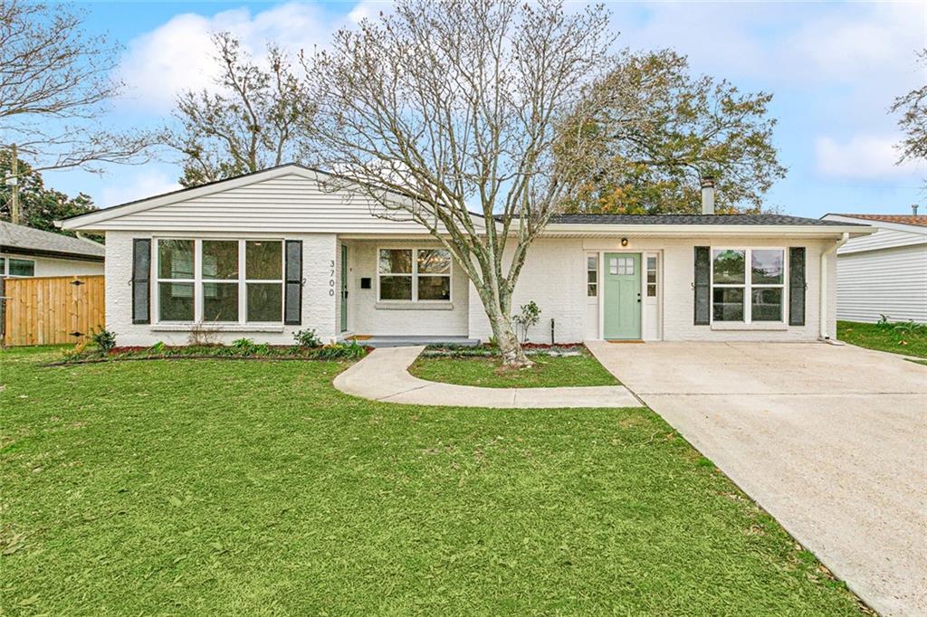 Single-story white brick house with black shutters, pale green door, and wide driveway.