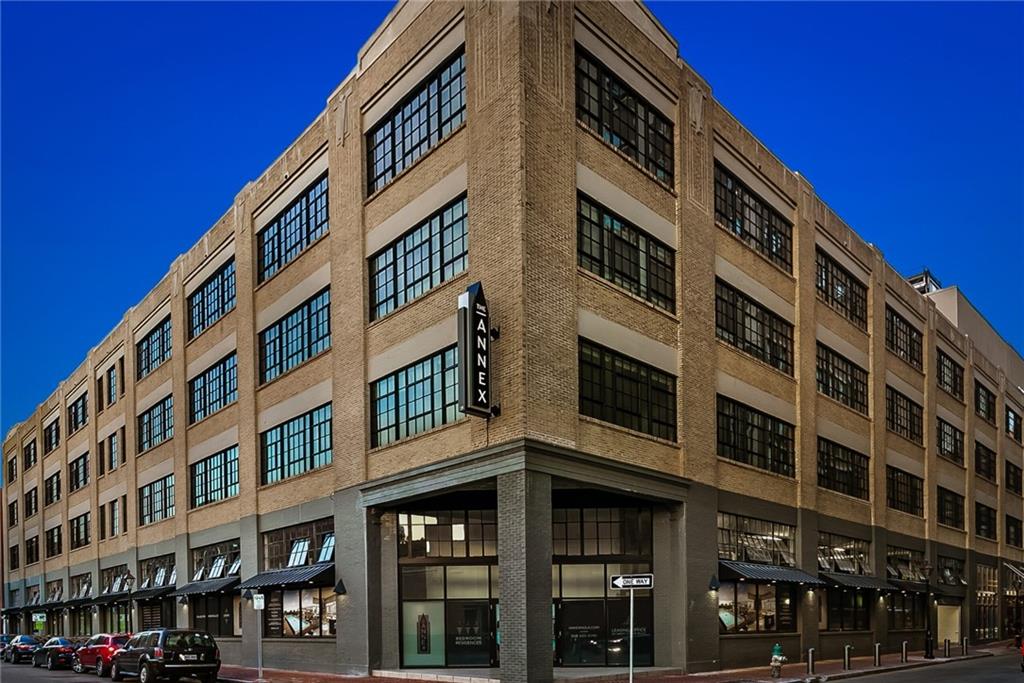 Tan brick commercial building with grid windows, storefronts, and a vertical ANNEX sign.