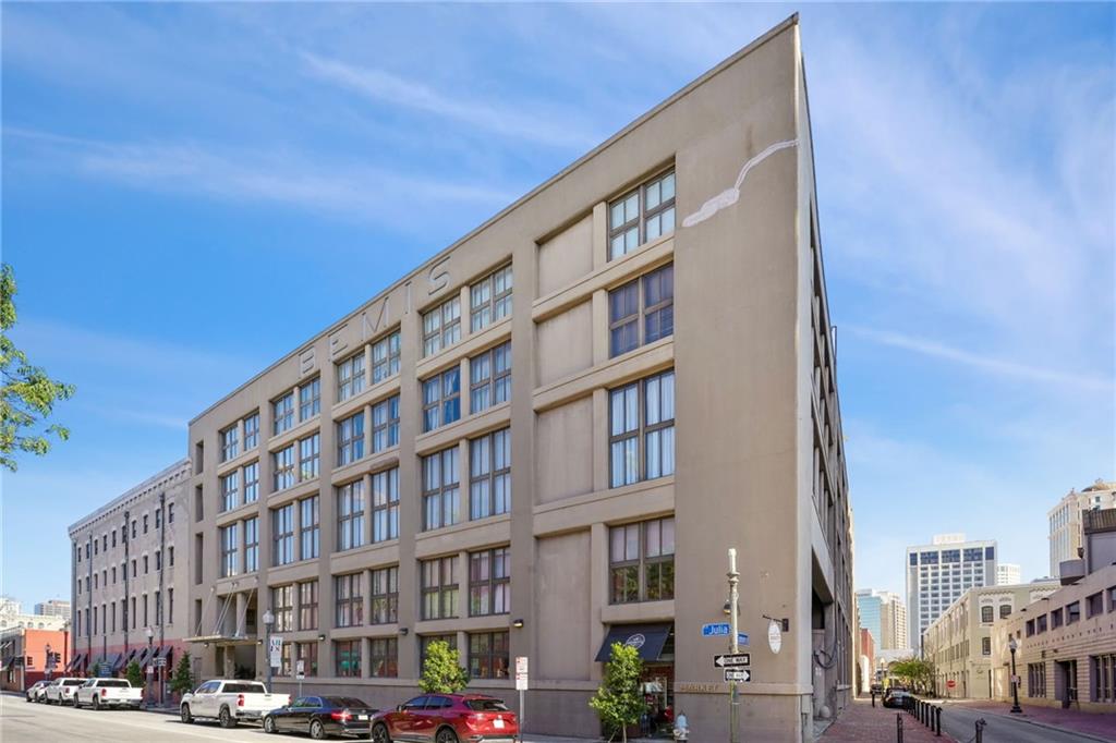 Beige multi-story corner building with rows of windows and parked cars along the street.